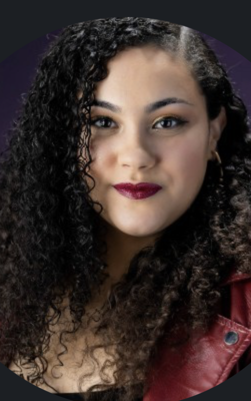Close-up of a woman with dark curly hair, wearing makeup with dark lipstick and a red leather jacket, against a dark background.