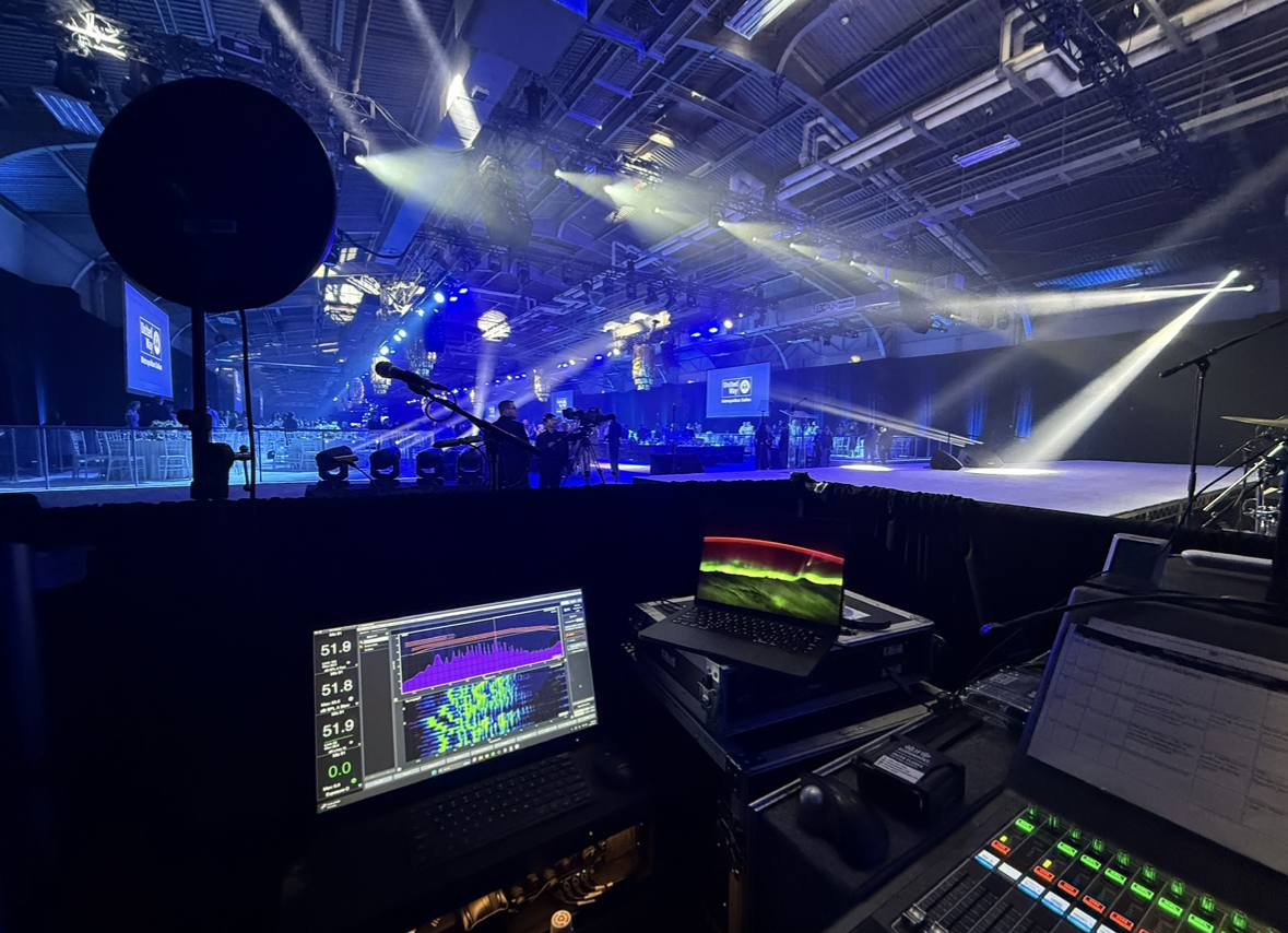 Stage with bright blue and white lighting, empty microphone on stand, and equipment at the front, possibly for a concert or event in a large indoor venue.