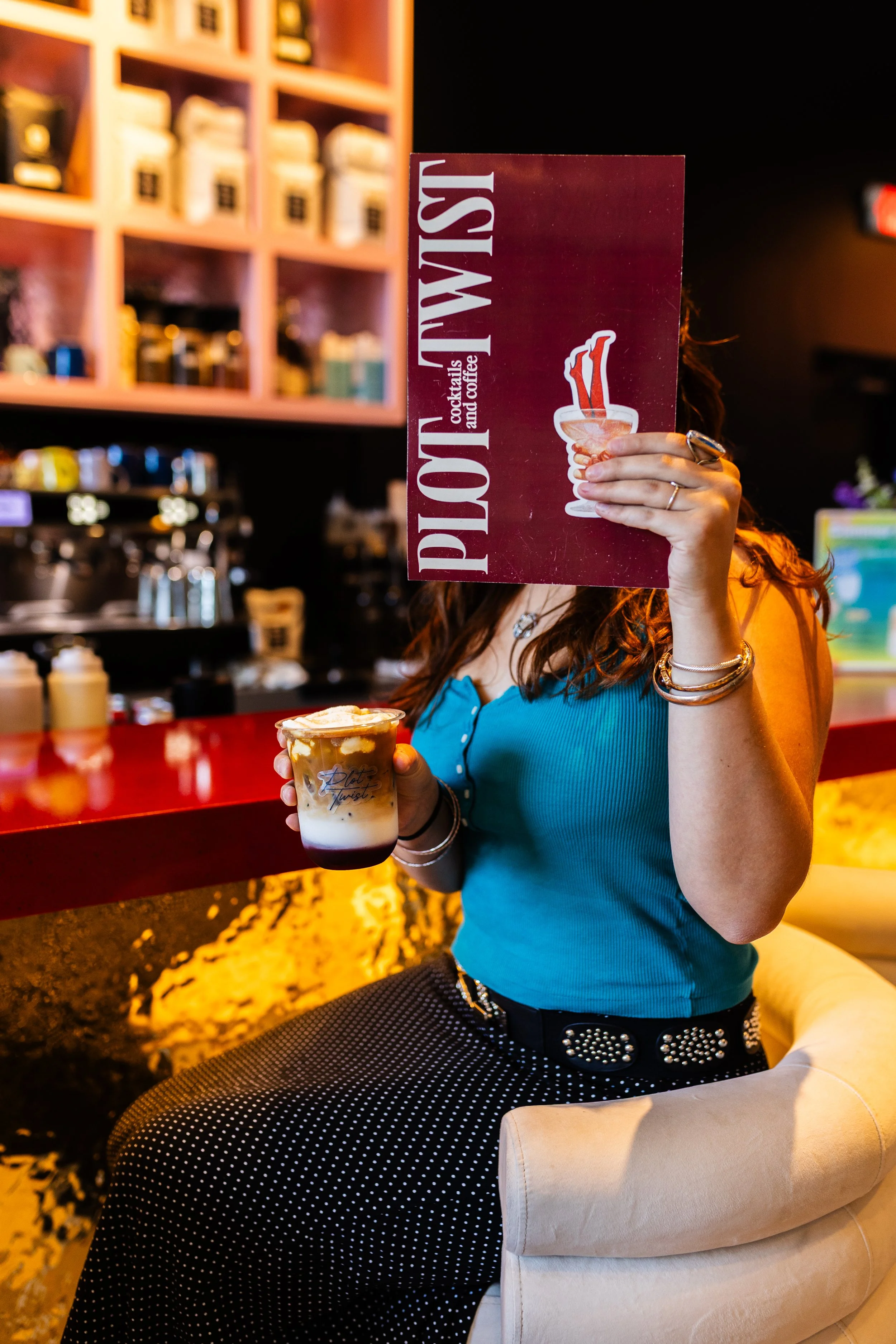 Person holding a coffee and Plot Twist menu at a coffee bar.