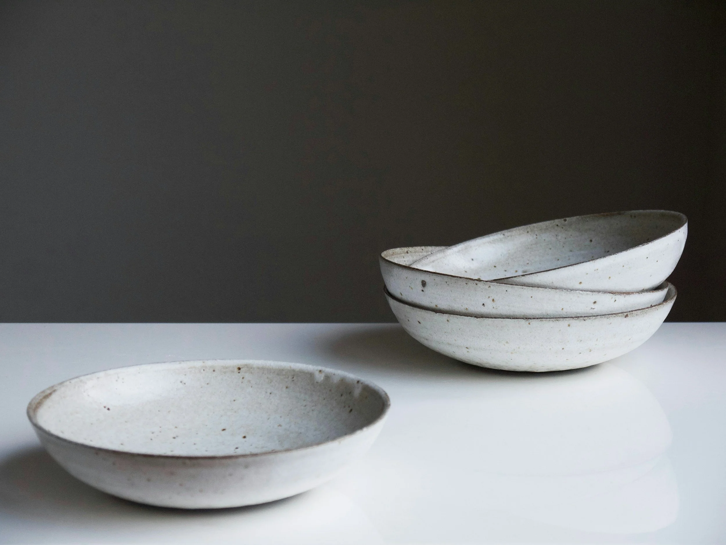 Stacked white ceramic bowls with black speckles, placed on a white surface against a dark background.