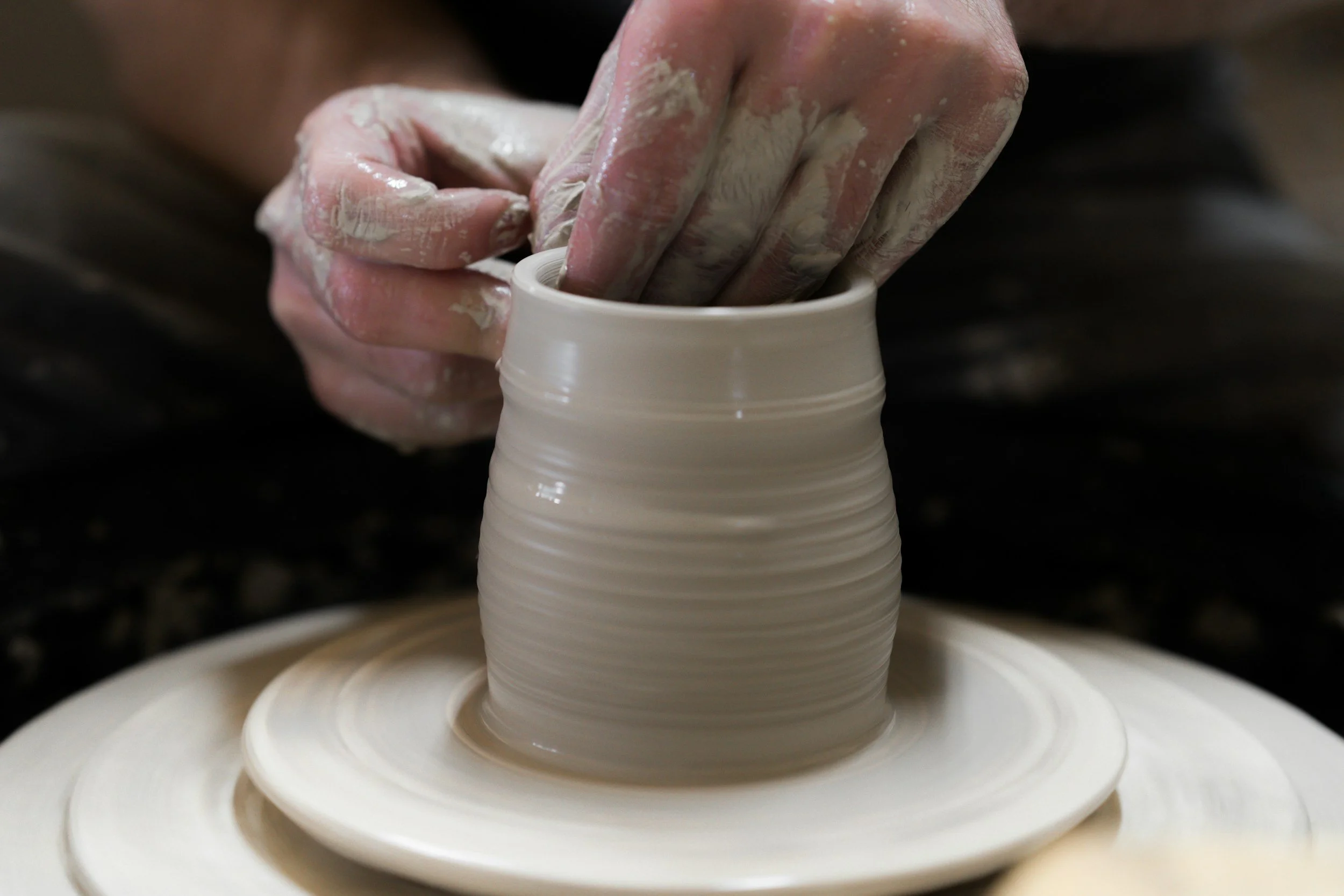 Close-up of hands shaping a pot on a spinning pottery wheel, with wet clay in a pottery studio.