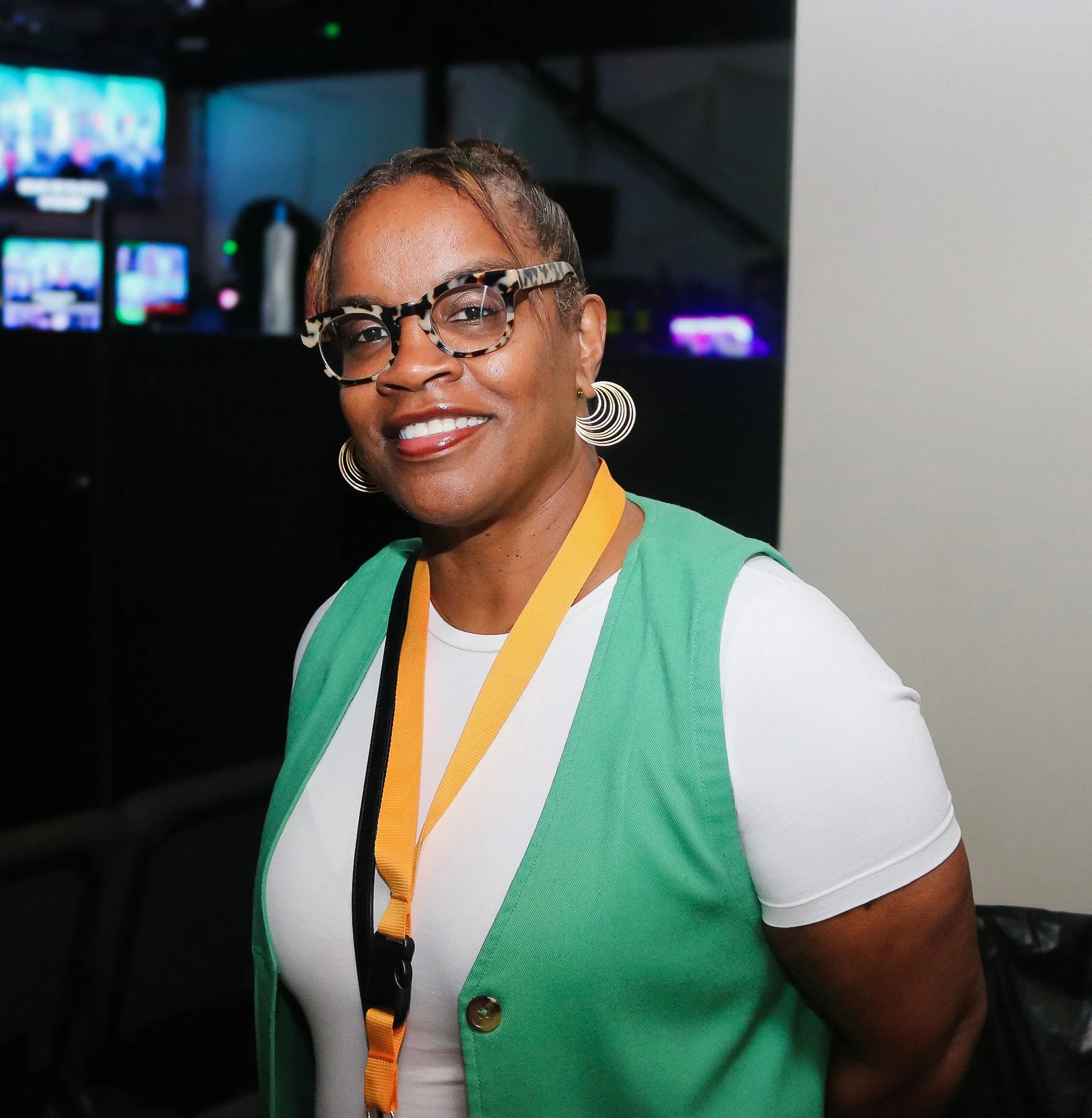 Smiling woman wearing glasses, a green and white top, and a lanyard.