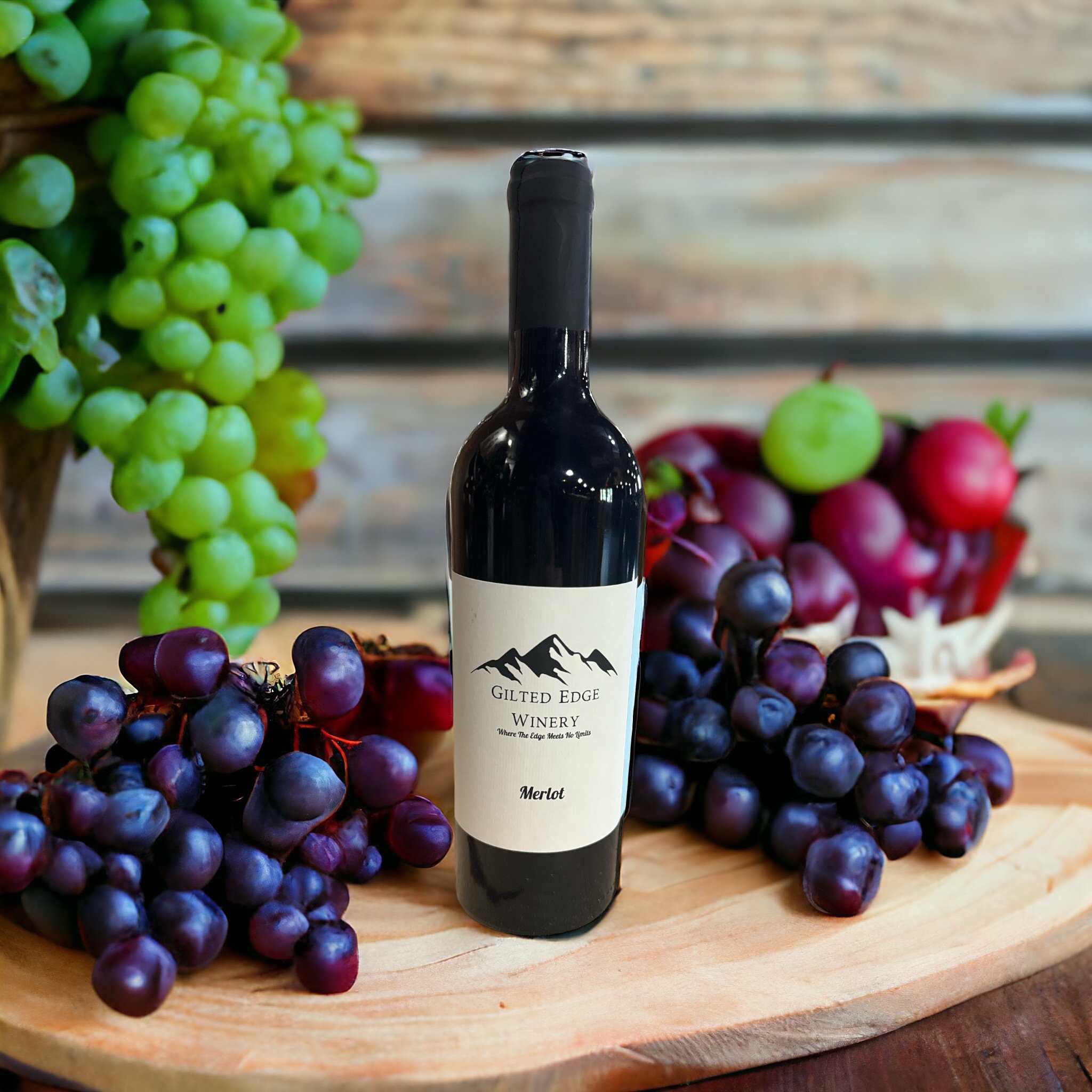 A bottle of Merlot red wine from Gilded Edge Winery stands on a wooden surface surrounded by green and purple grapes.