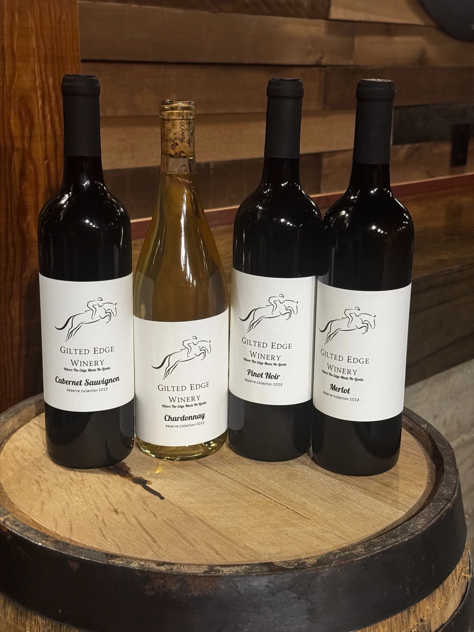 Four bottles of wine from Gilded Edge Winery, including Cabernet Sauvignon, Chardonnay, Pinot Noir, and Merlot, are displayed on a wooden surface.
Reserve Collection