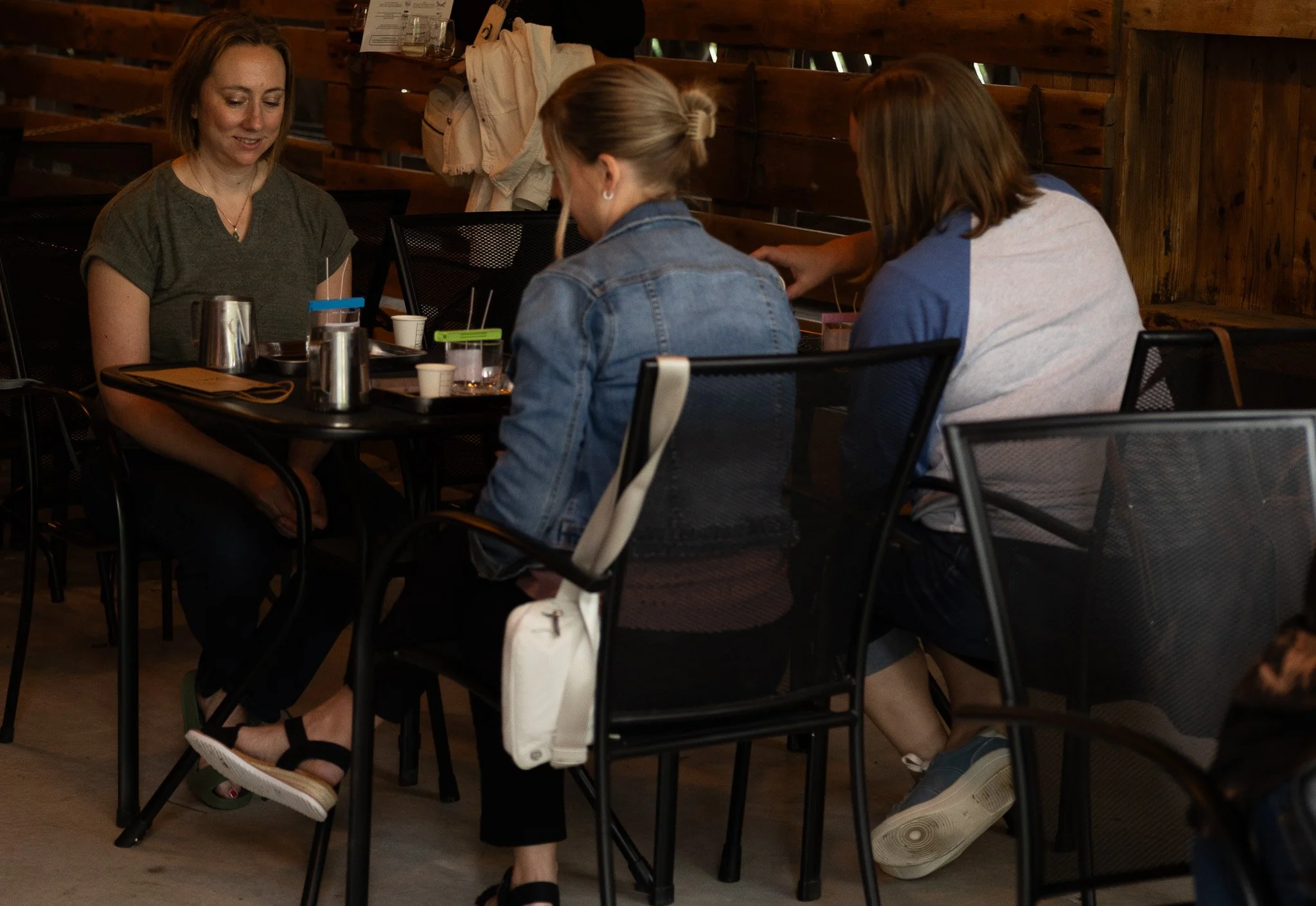 Three women sitting at a table in a restaurant, looking at their phones and talking.
