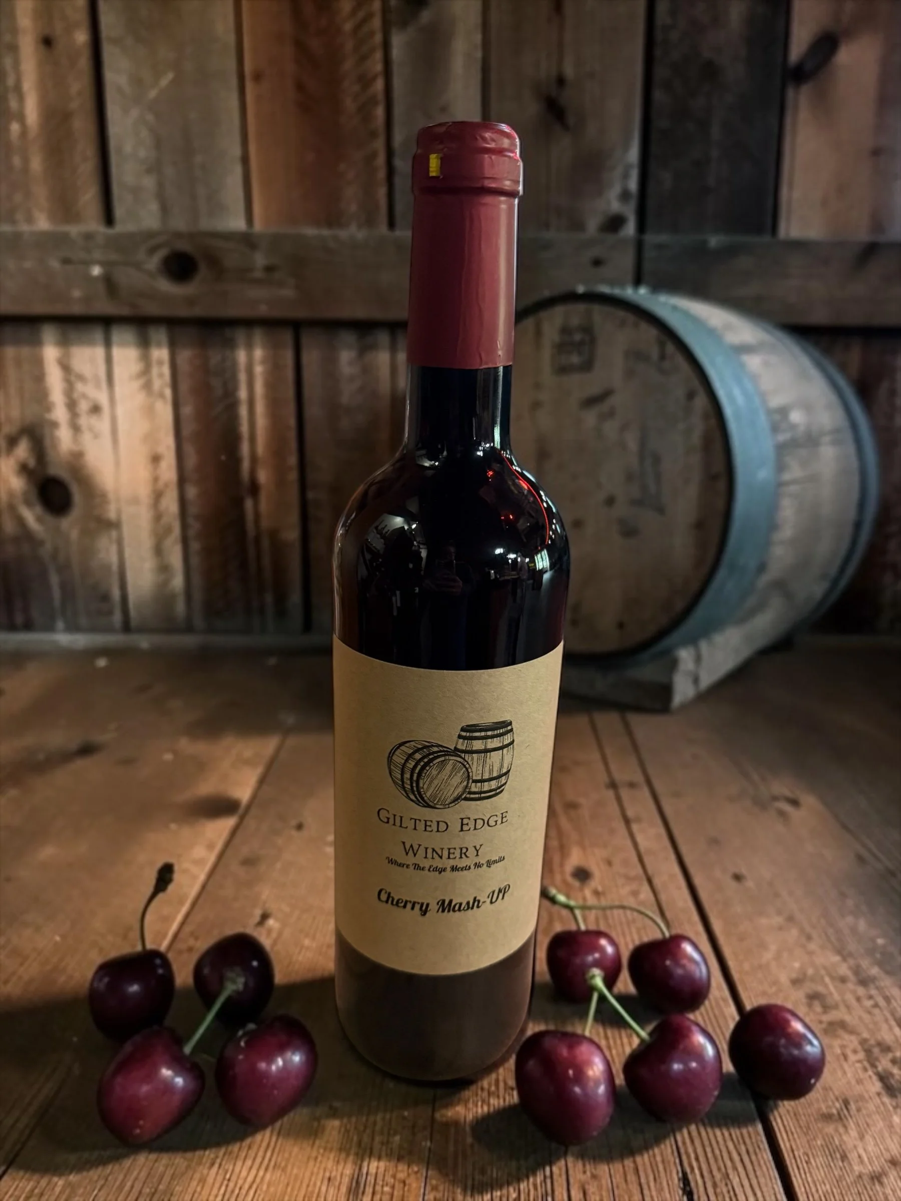 A wine bottle labeled 'Gilded Edge Winery' with cherries arranged around its base, set against a wooden background with a wine barrel in the back.