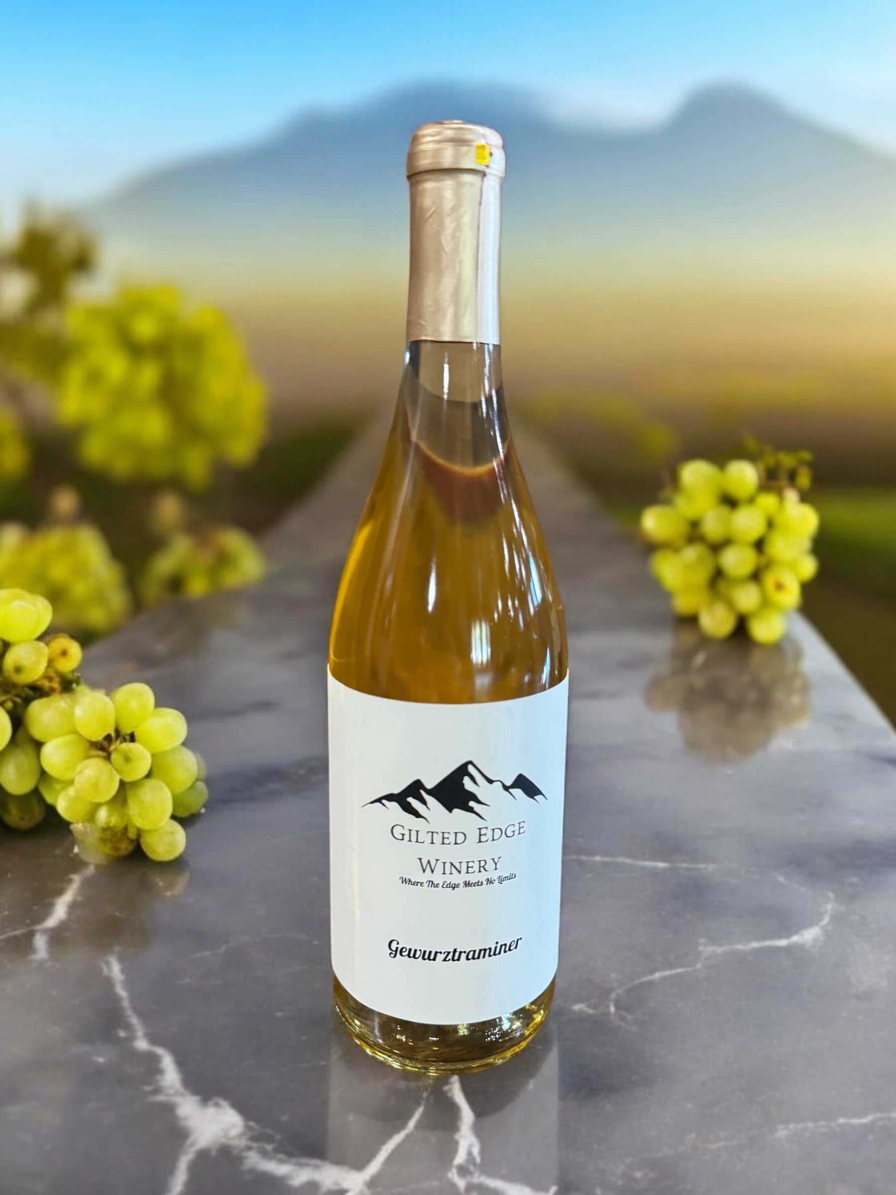 A bottle of Gewurztraminer wine with a mountain logo label from Gilt Edge Winery on a marble surface, with yellow-green grape clusters in the background.