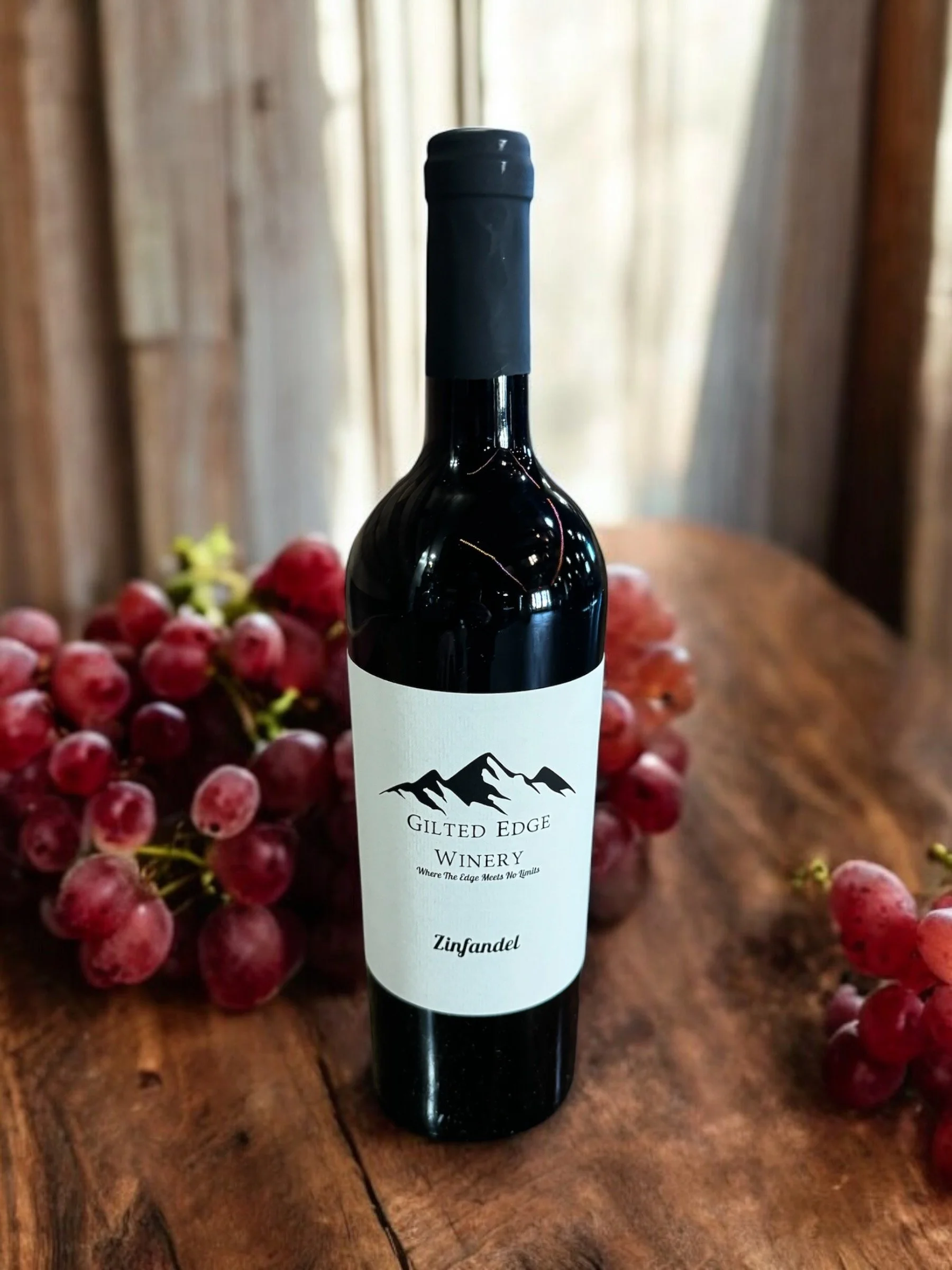 A bottle of Zinfandel wine from Gilded Edge Winery, with grapes in the background on a wooden surface.
