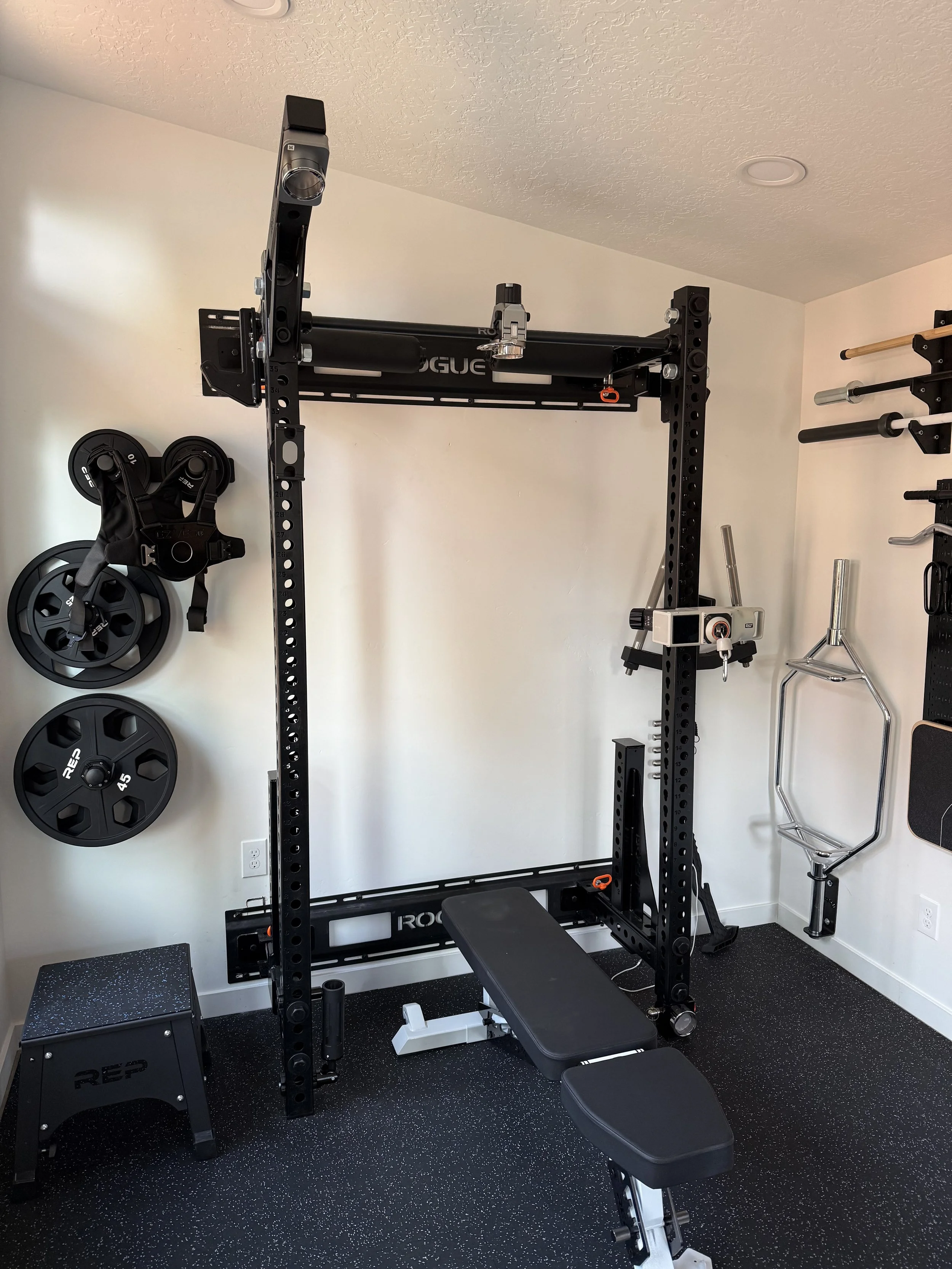 A home gym with a black power rack, weight plates mounted on the wall, a black workout bench, and various workout equipment on the walls.