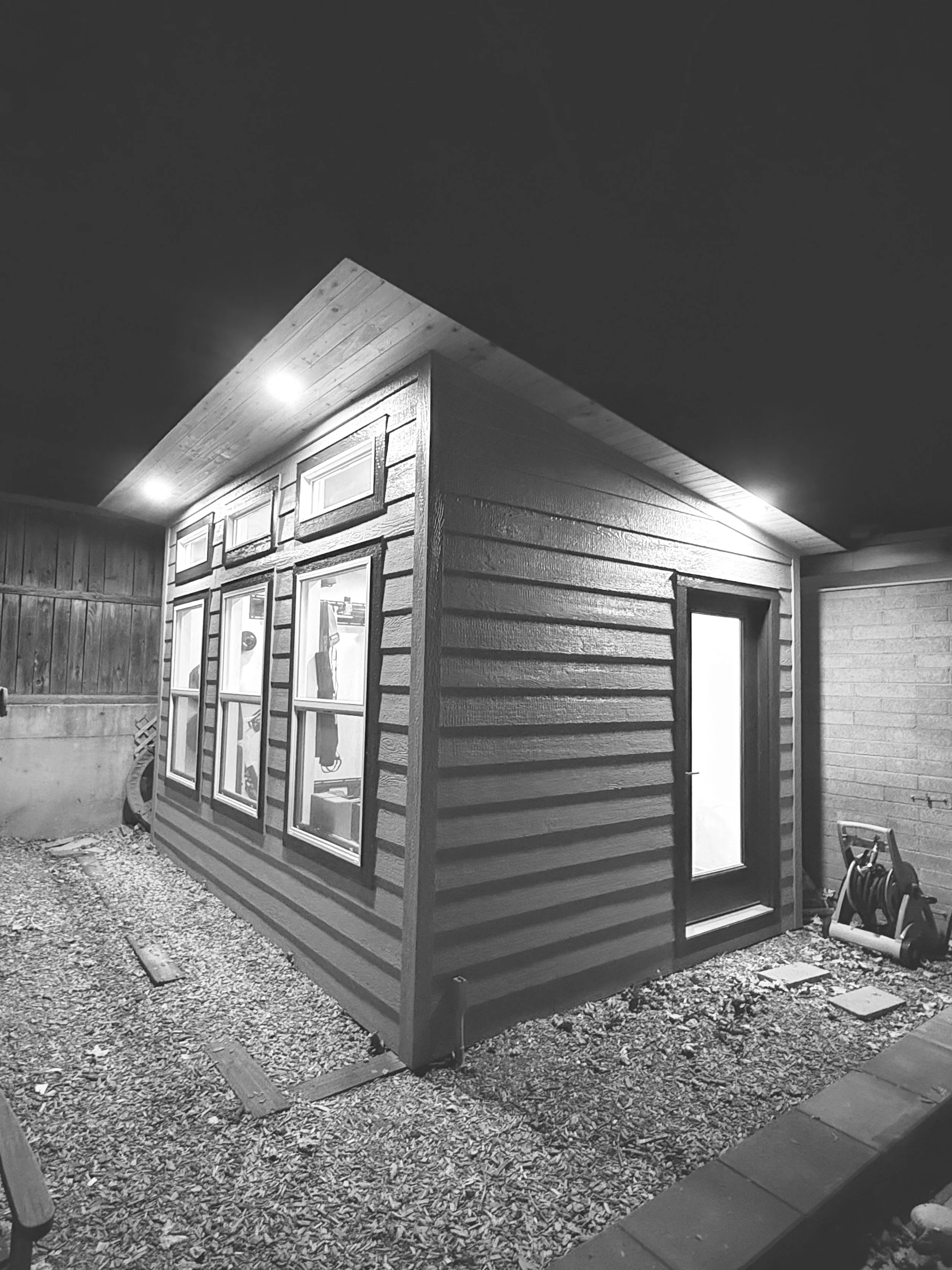 Exterior view of a studio at night with illuminated windows and a sloped roof, black and white photo.