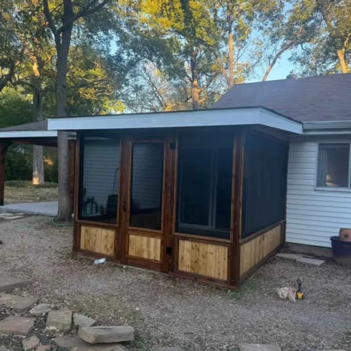 Backyard with a newly built screened porch with wooden frame attached to a house with white siding and surrounded by trees.