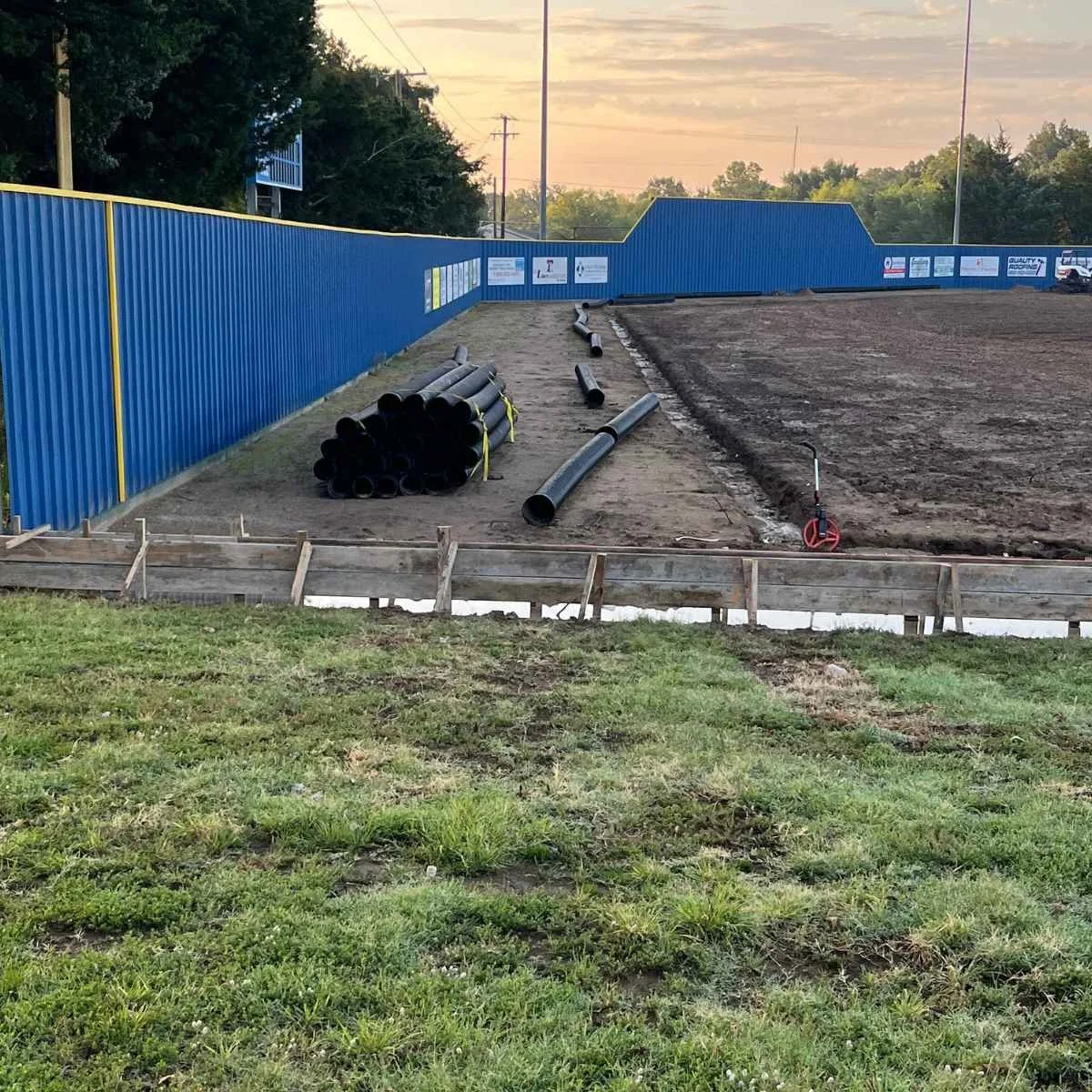 Construction site with black pipes stacked on gravel during an irrigation installation project on an athletic field in Paris, Texas.