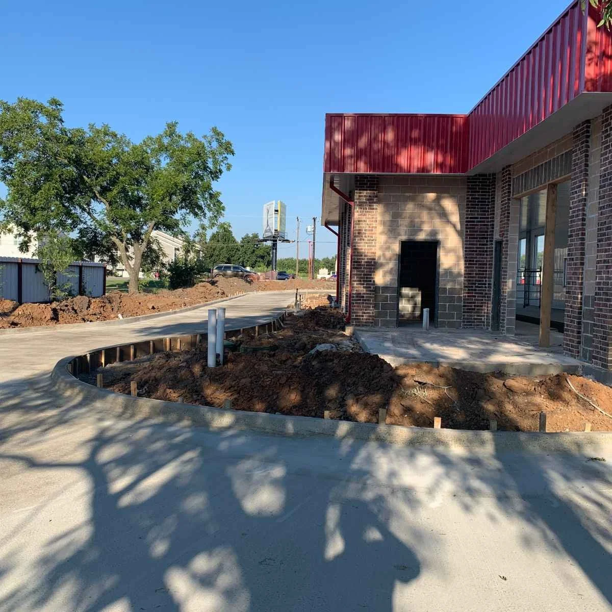 Construction site with a partially built brick building, dirt, and a newly poured sidewalk preparing for irrigation system installation. 