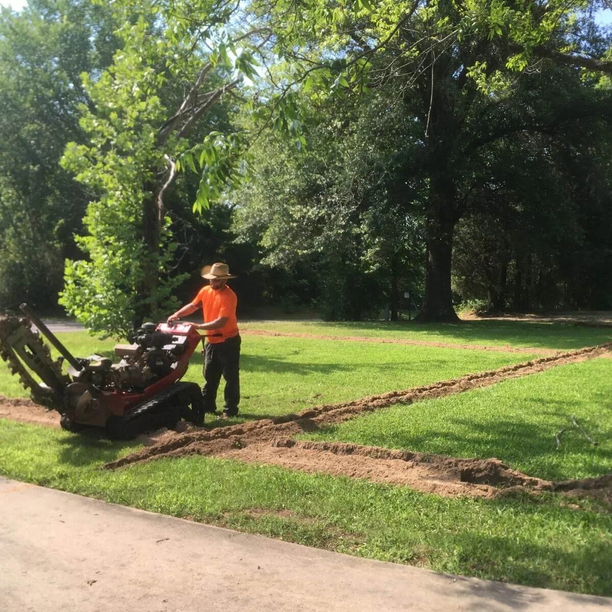 A person operating a trenching machine at a residential home preparing for irrigation work.