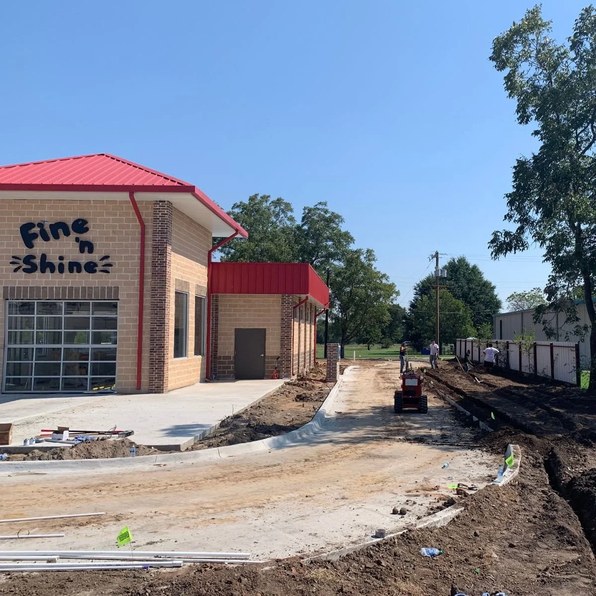 Commercial building under construction, with partially paved driveway, construction workers, and construction equipment during sprinkler installation in northeast Texas.