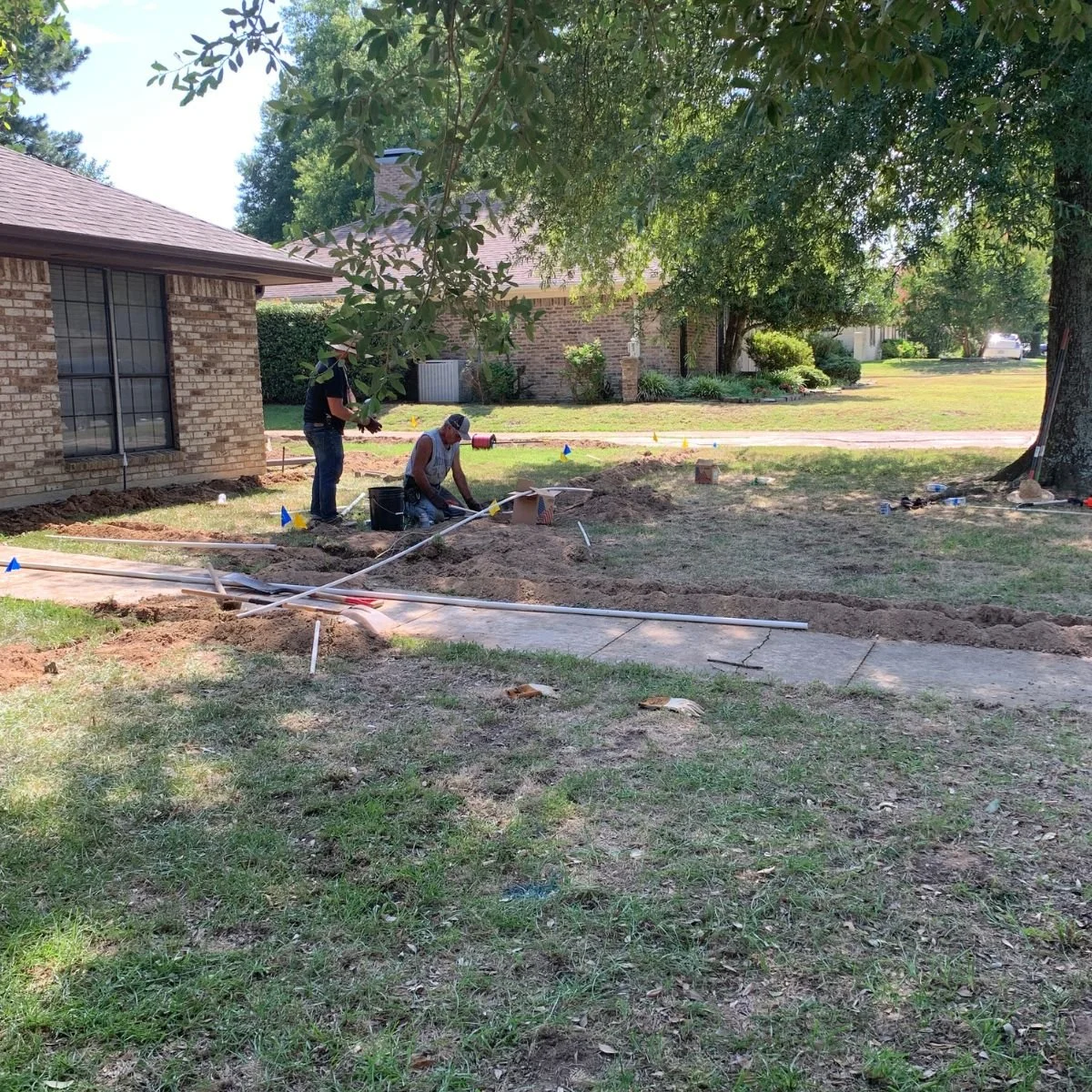 Two workers installing or repairing sprinklers in a residential yard in northeast Texas.