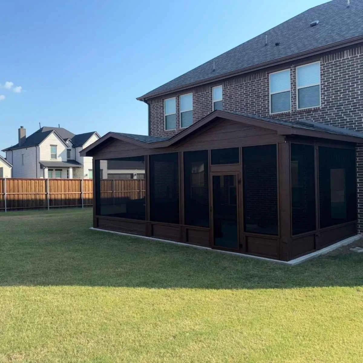 Backyard with a screened-in porch attached to a brick house, surrounded by a wooden fence.