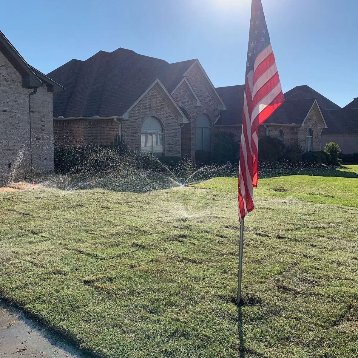 Sprinkler system watering the grass at a brick home in northeast Texas