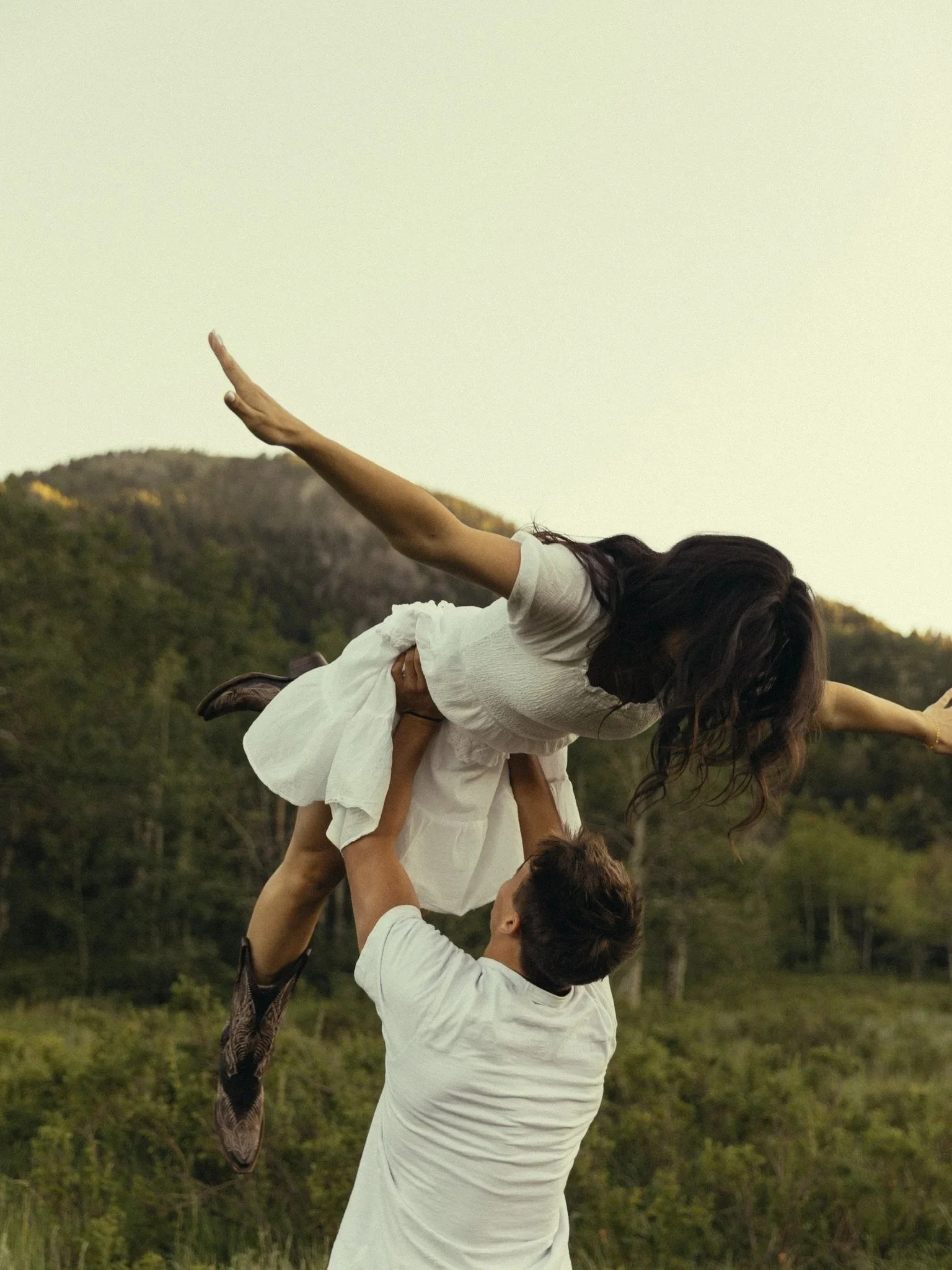 A group of people outdoors, forming a human pyramid against a backdrop of trees and hills.