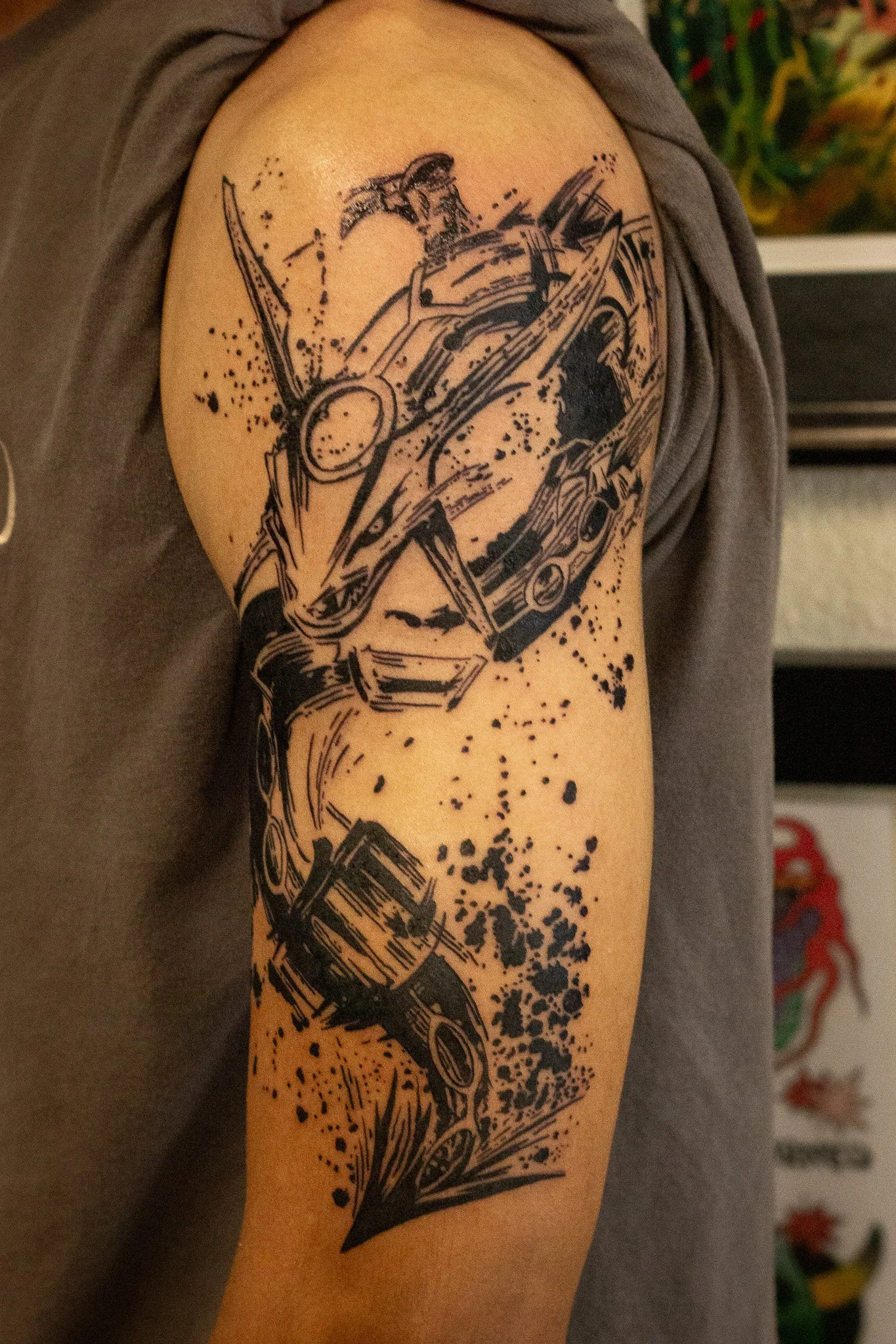 Black ink tattoo of musical instruments with splatter design on upper arm.