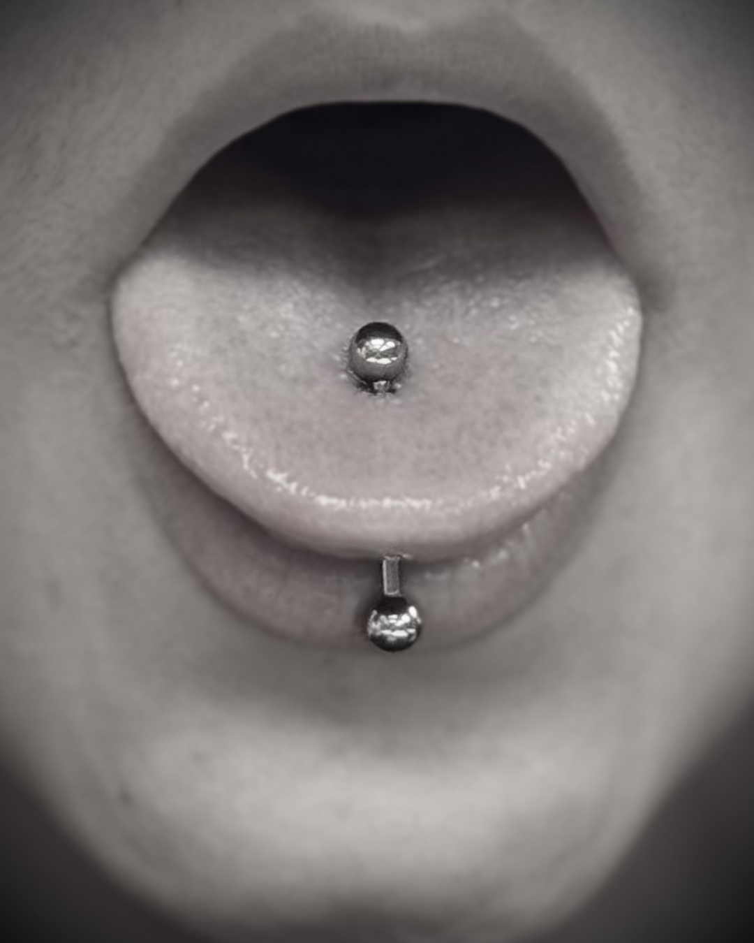 Close-up of a person's tongue with a tongue piercing that has two metallic balls, one on the top and one on the bottom.