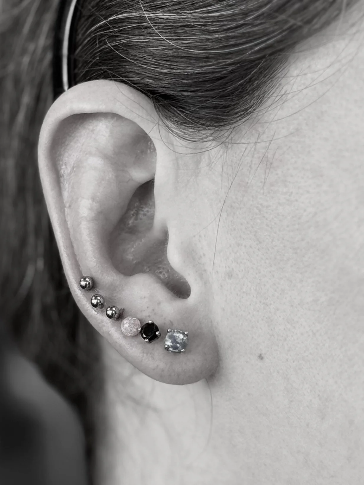 Close-up of a person's ear with multiple earrings, including small balls, a black gem, and a large clear stone.