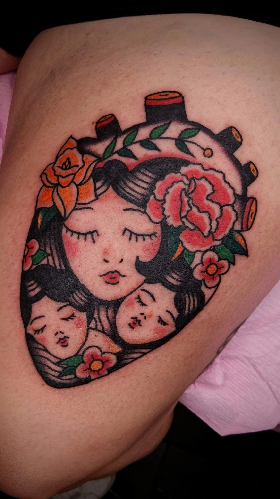 A tattoo of a woman with her eyes closed and flowers and leaves in her hair, surrounded by smaller faces with closed eyes.
