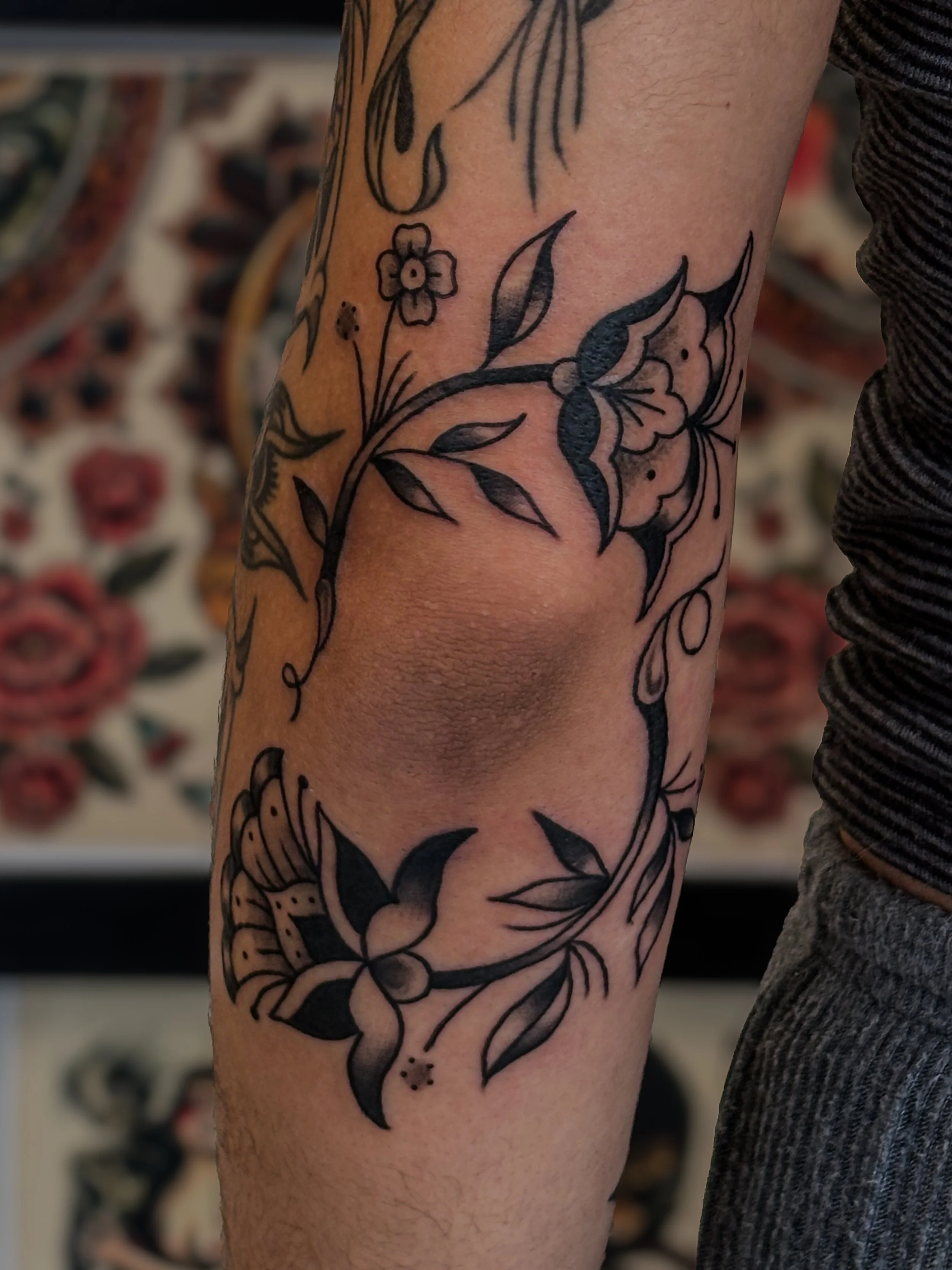 A person's arm with a black and white floral tattoo featuring leaves and small flowers.