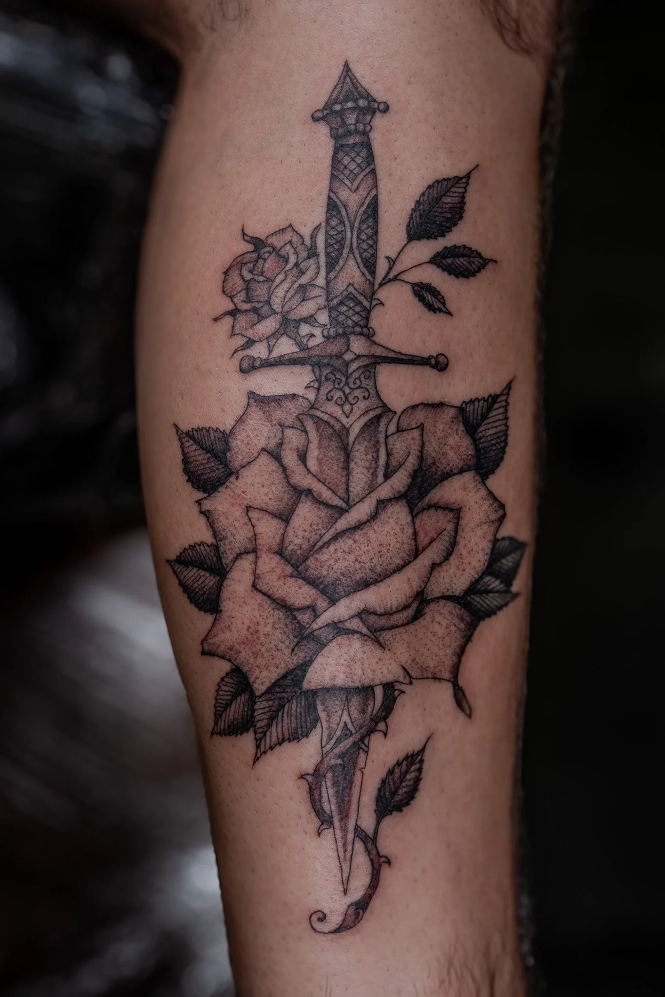 Tattoo of a knife with roses and leaves on a person's arm.