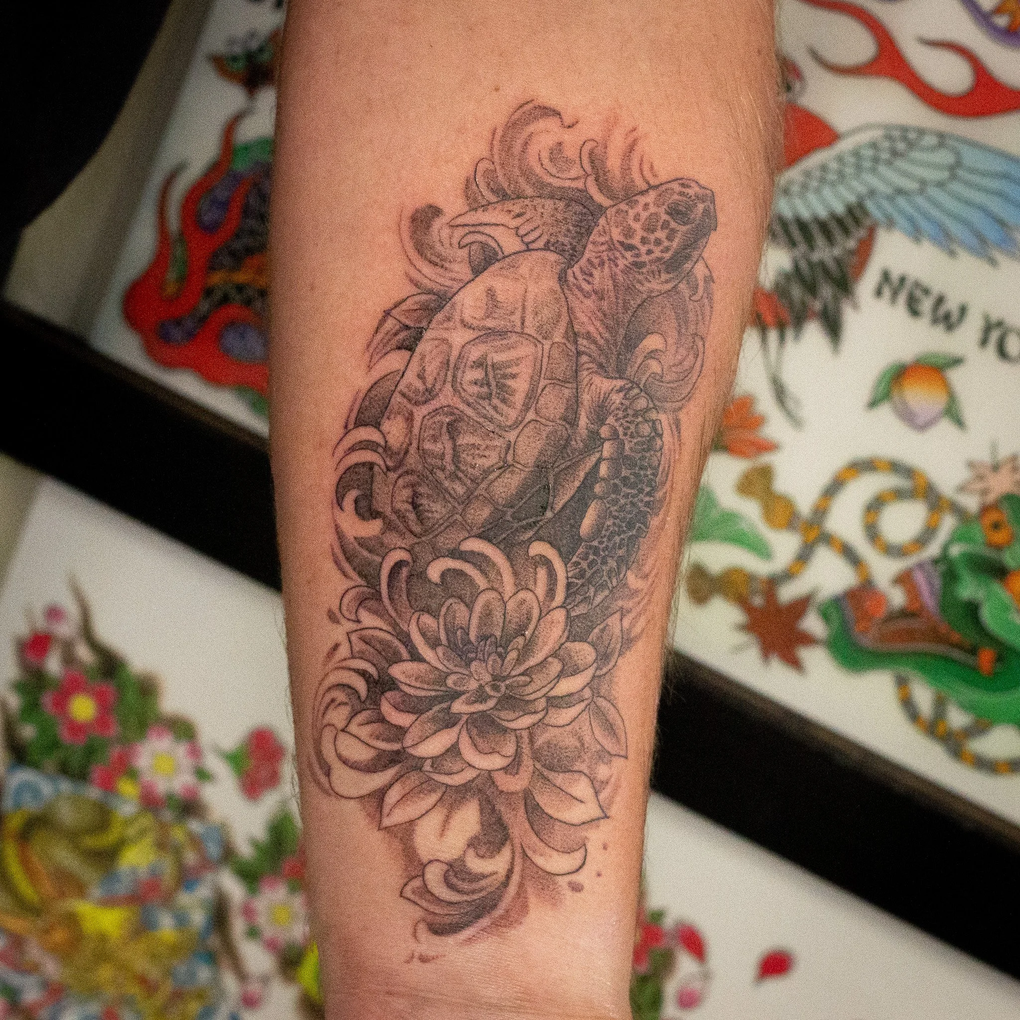 Tattoo of a sea turtle with detailed petals and leaves on someone's forearm.