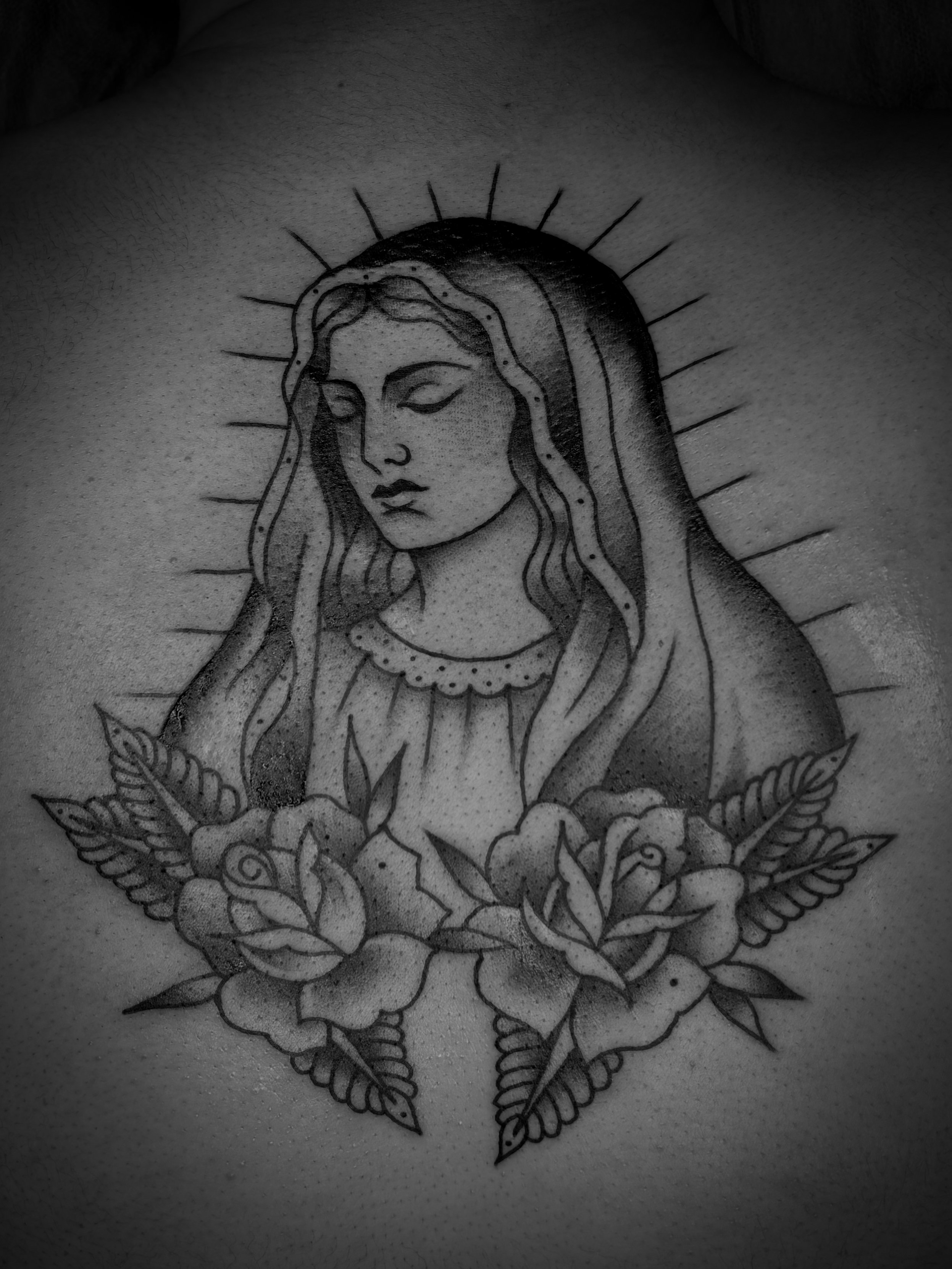 Black and white tattoo of a woman with a serene expression, surrounded by a halo and floral motifs.
