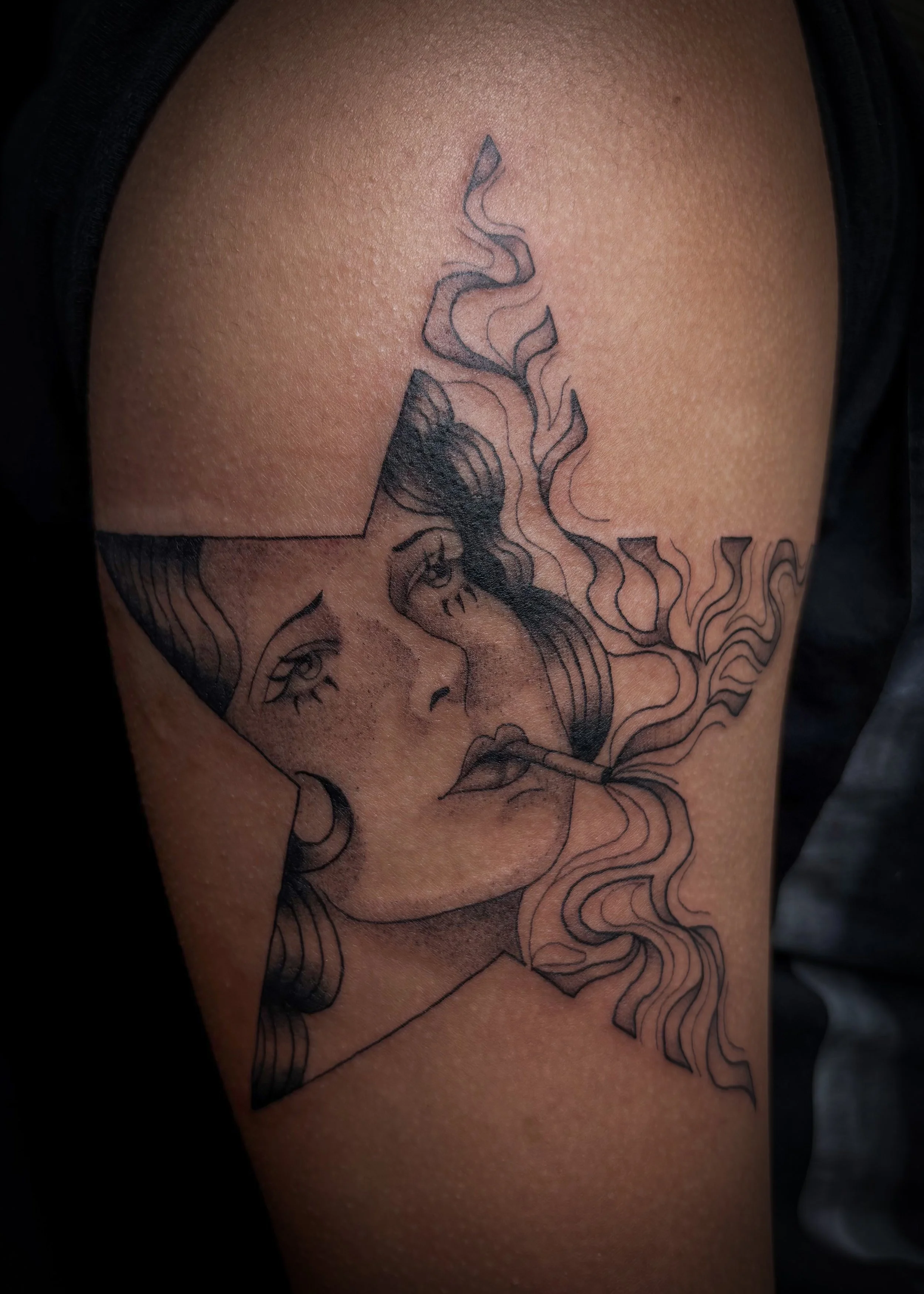 Tattoo of a woman smoking with smoke rising from a star, with a face and hair, on a person's upper arm.