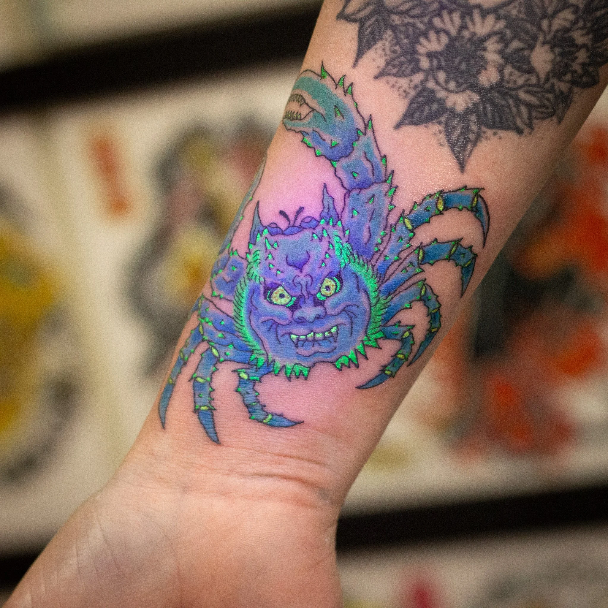 UV Black Light Tattoo of a japanese crab with vibrant blue, green, and purple colors on a person's forearm.