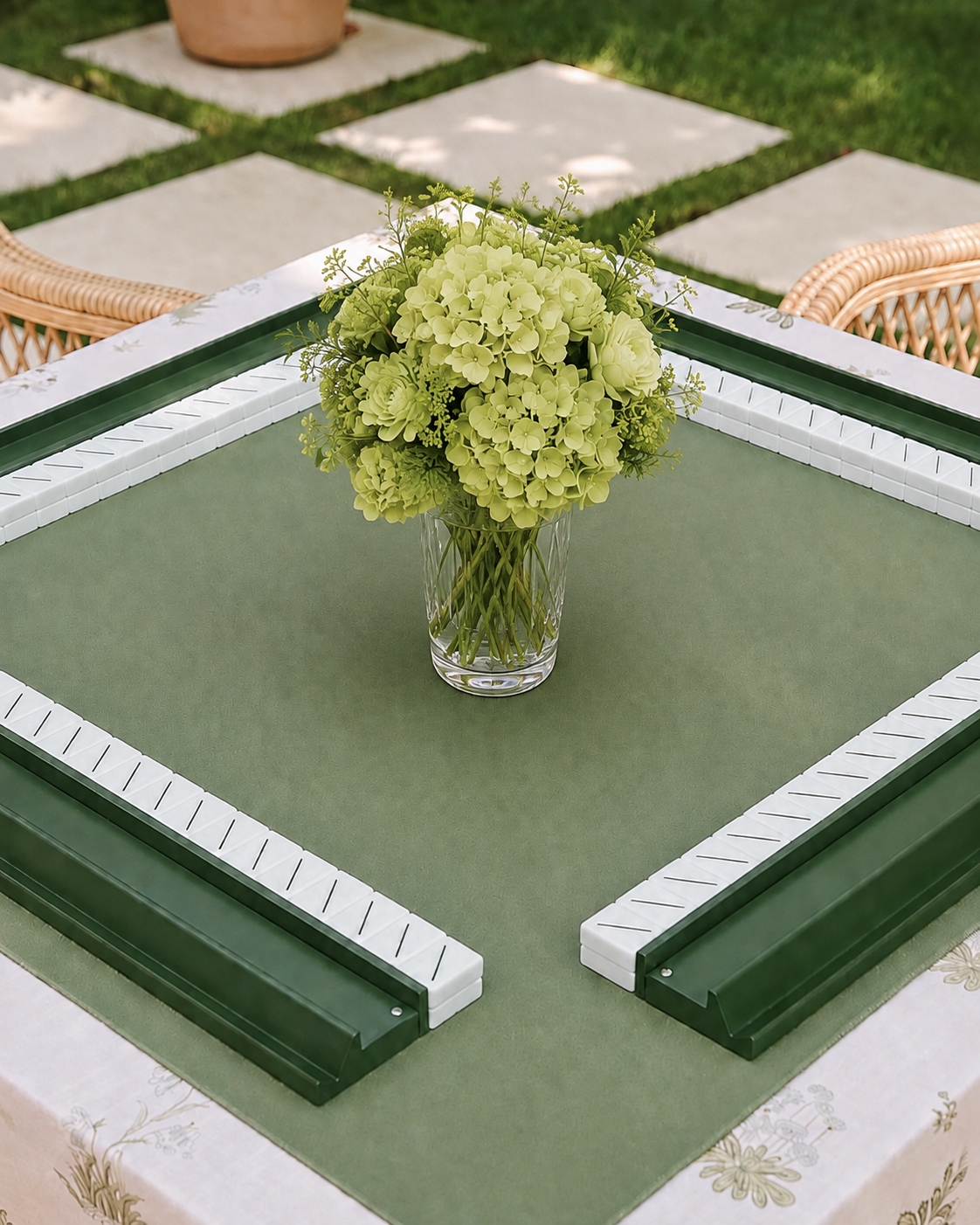 A vase with a bouquet of yellowish-green hydrangeas on a game table with a green felt surface, surrounded by white and dark green border pieces, outdoors on a patio.