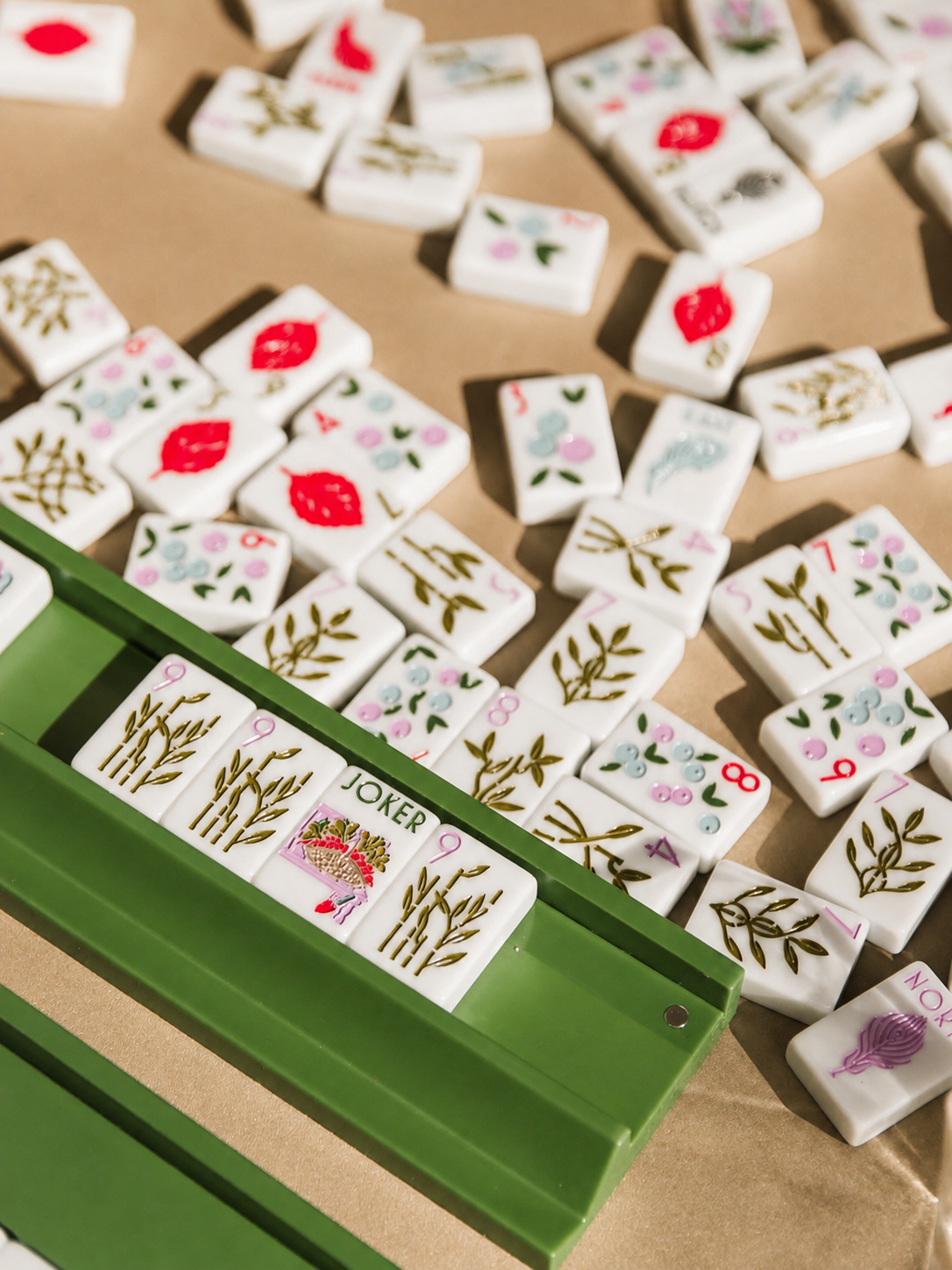 Decorative dominoes with floral, leaf, and abstract patterns scattered on a surface, with a green box holding a few dominoes, including a Joker tile.