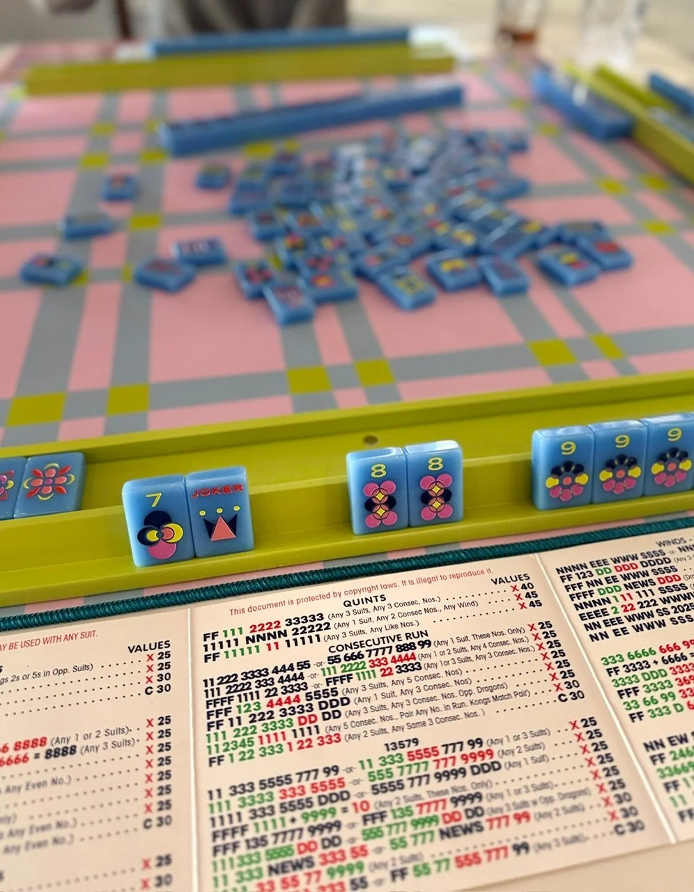 Close-up of a game of dominoes with blue tiles and a game board, with a sheet of rules and scores underneath.