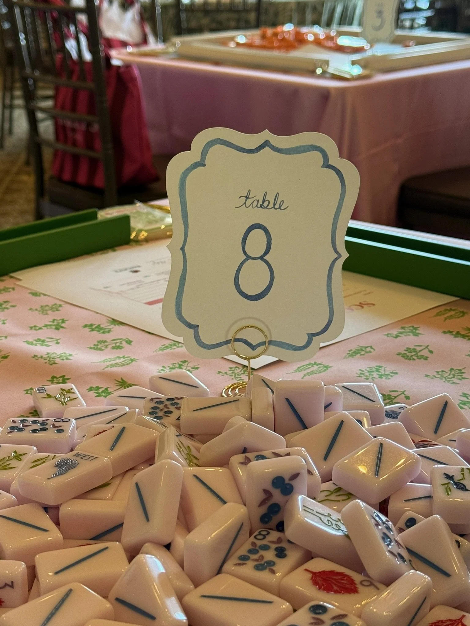 A table number card with the number 8 on it, placed among domino tiles on a decorated table at a social gathering.