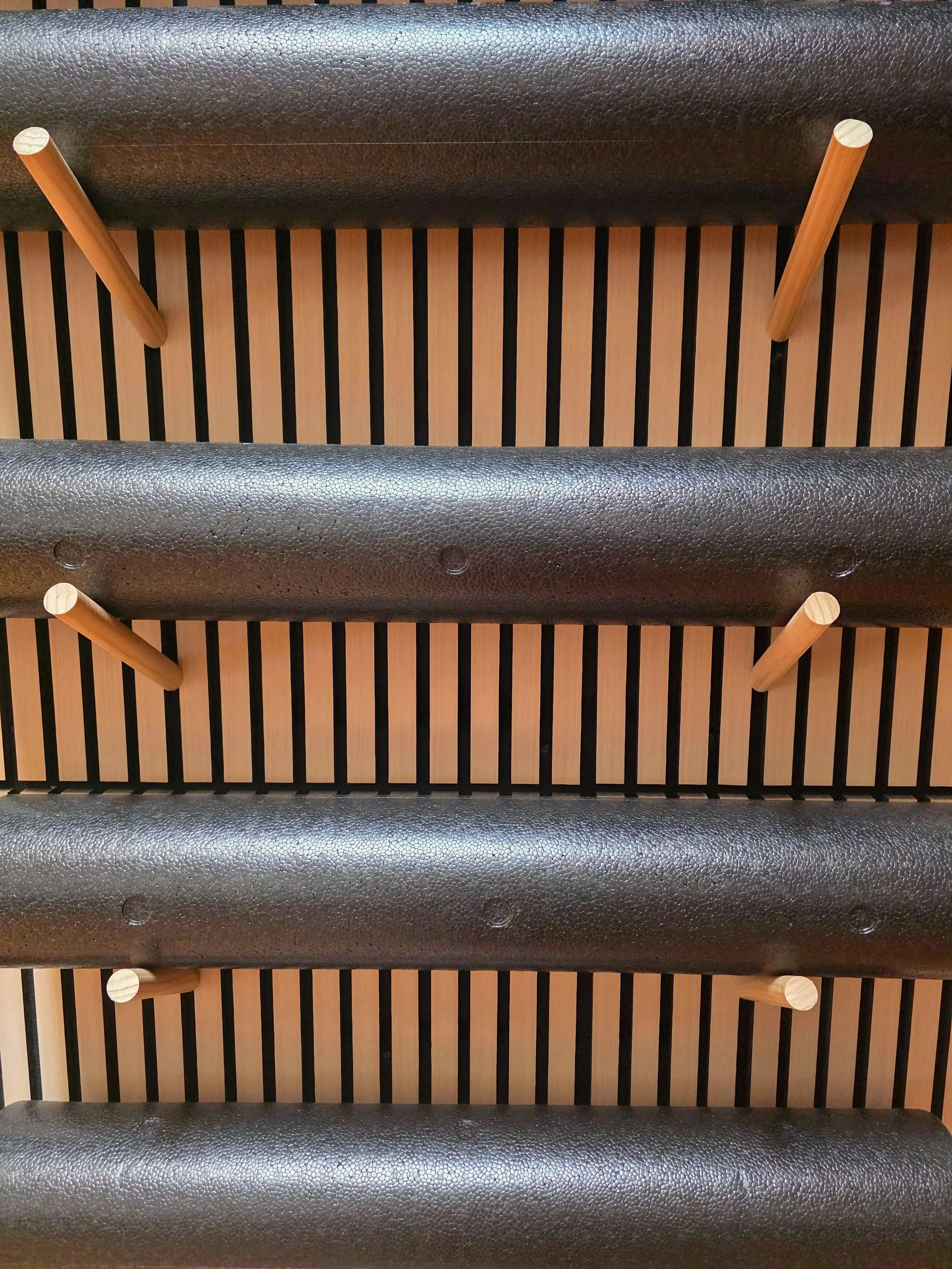 Close-up of black foam rollers hanging on a light-colored acoustical wood paneled wall.