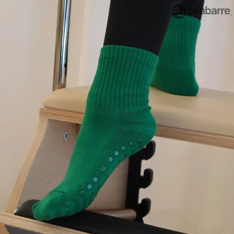 Close-up of a person wearing green Pilates grippy socks standing on a beige cushioned surface.