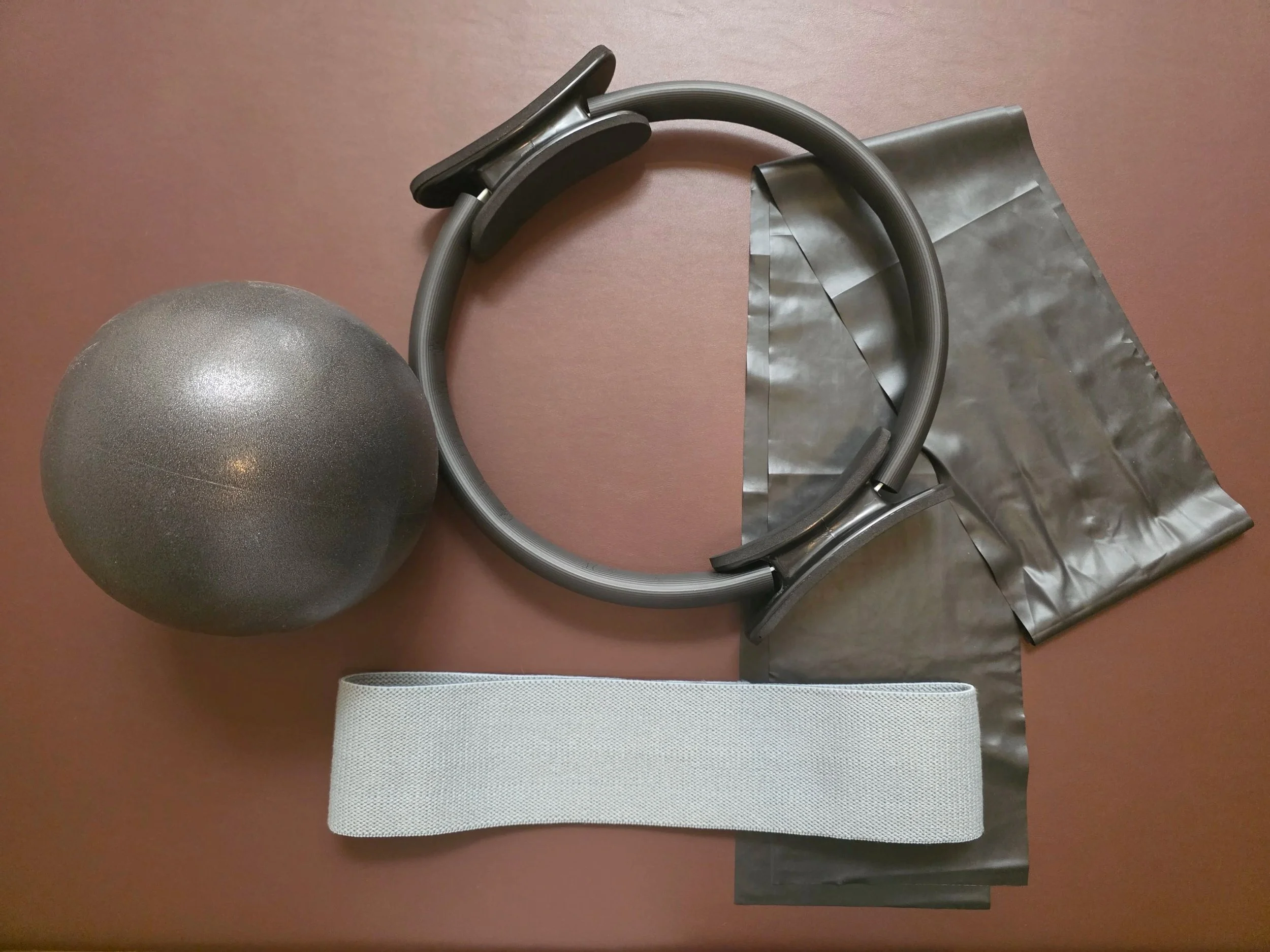 Fitness equipment including a gray exercise ball, a flexible gray Magic Ring, grey thigh resistance bands, and black silicone theraband.