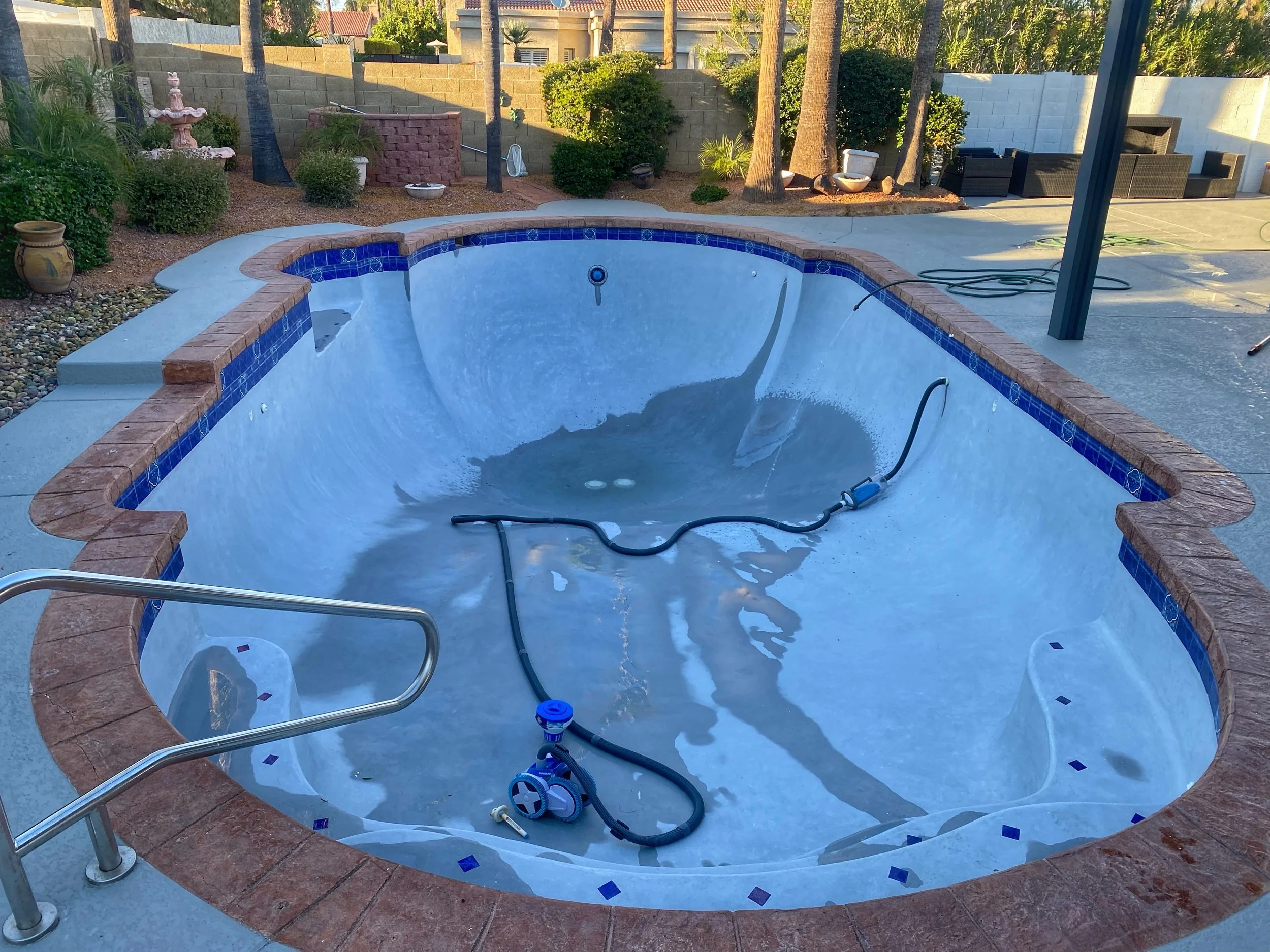 Empty backyard hot tub with pool cleaning equipment and fully landscaped yard with trees, bushes, and outdoor seating area.