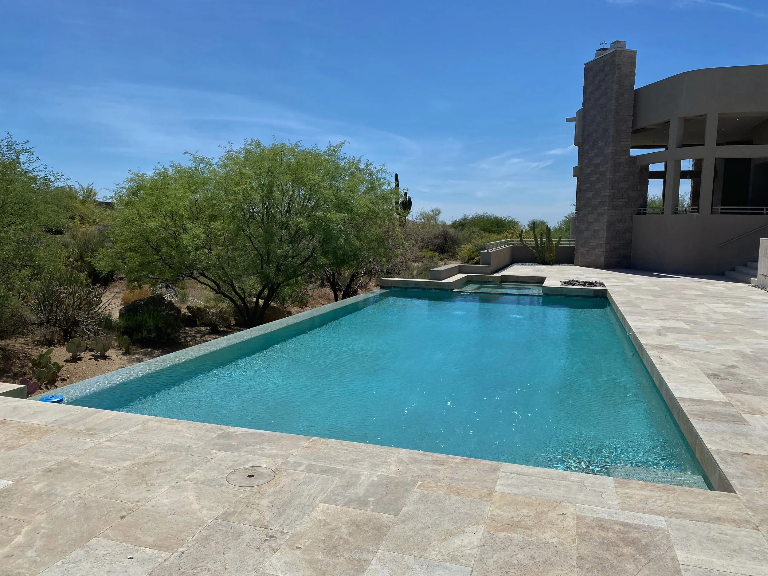 A modern house with a pool in a desert landscape, surrounded by cactus and desert plants, under a clear blue sky.
