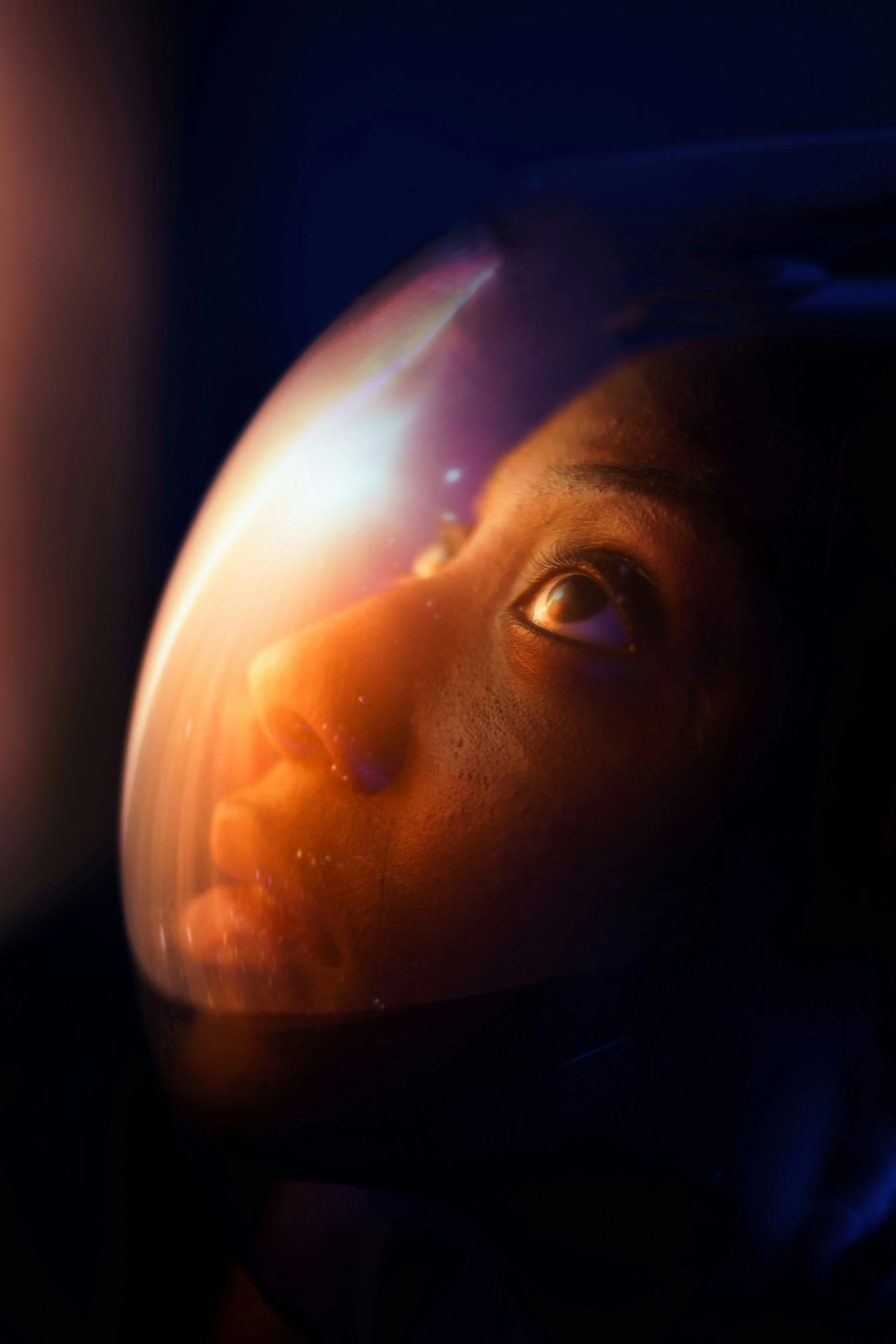 Close-up of a human face looking upward with part of the face lit by an orange glow of space