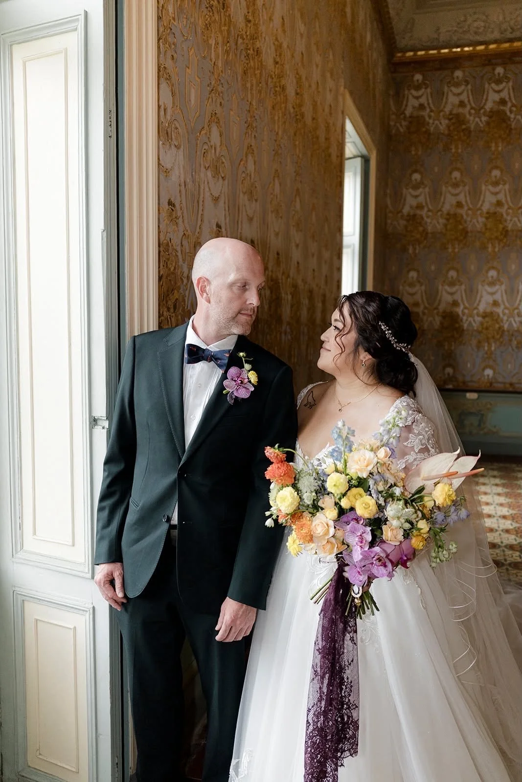 Candid portrait of a bride and groom during a destination wedding, showcasing a modern pastel floral bouquet and matching orchid boutonniere.