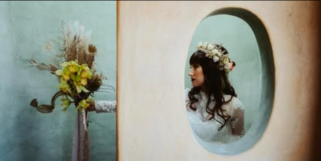 Artistic mirror reflection of a bride wearing a white rose floral crown next to a modern dried botanical bouquet.