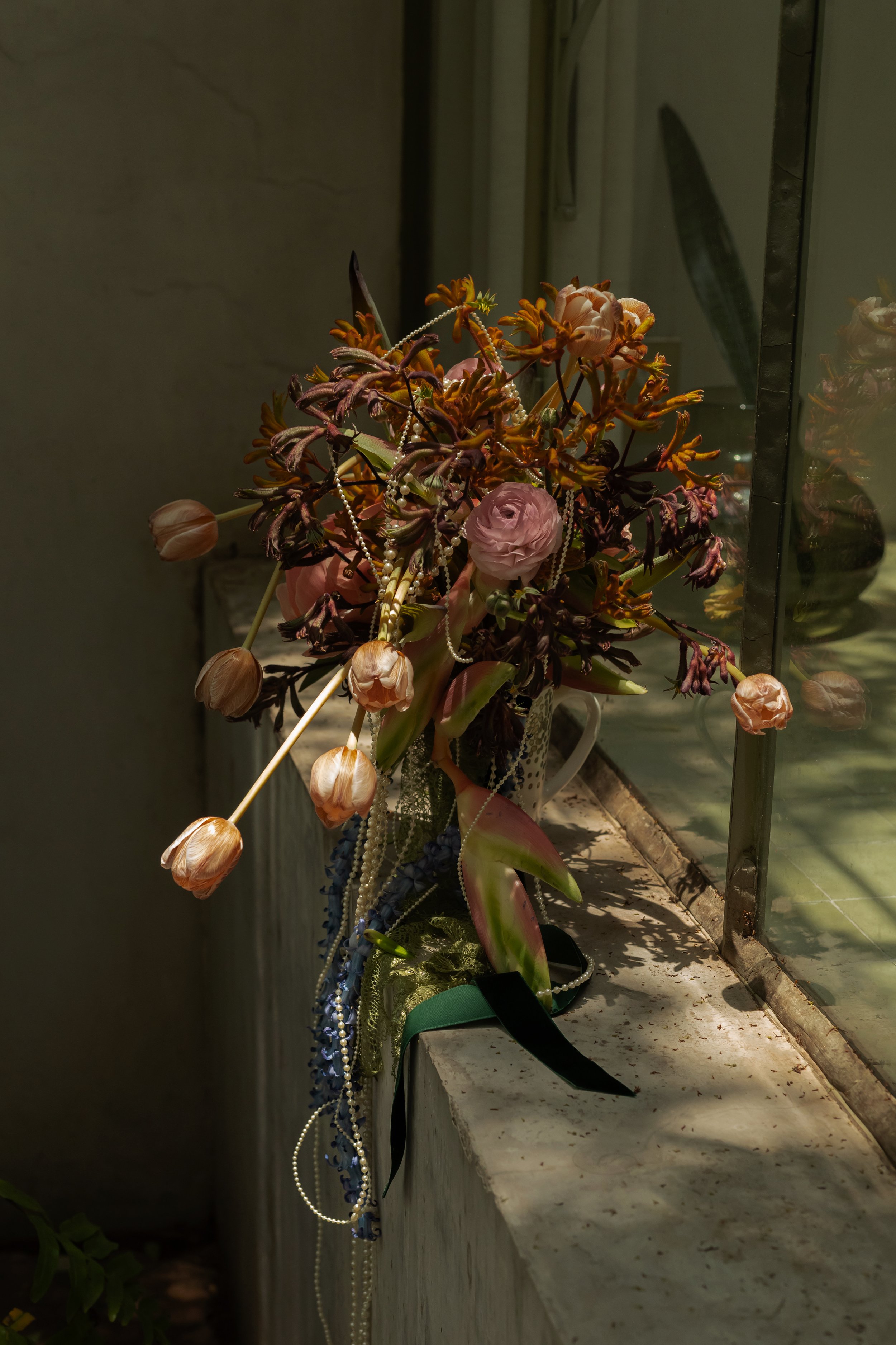 Artistic close-up of an editorial wedding bouquet with pearls and velvet ribbons on an ancient window ledge for the Inquire page.