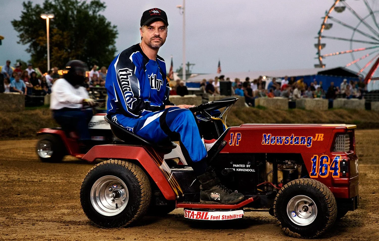 Racer in uniform on a modified racing lawnmower at a county fair, editorial portrait by Michael Rudin