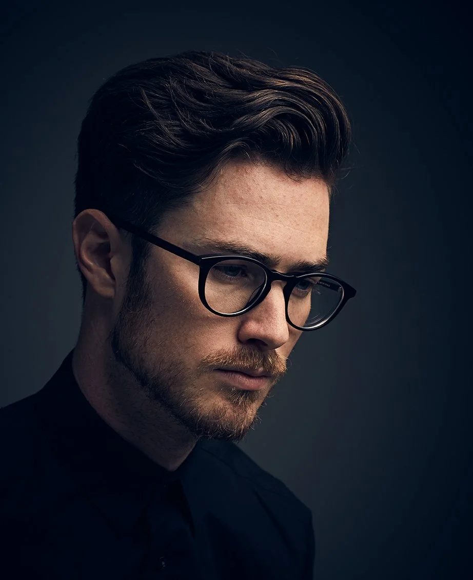 Editorial close-up portrait of a man wearing glasses in dramatic side lighting, photographed by Michael Rudin