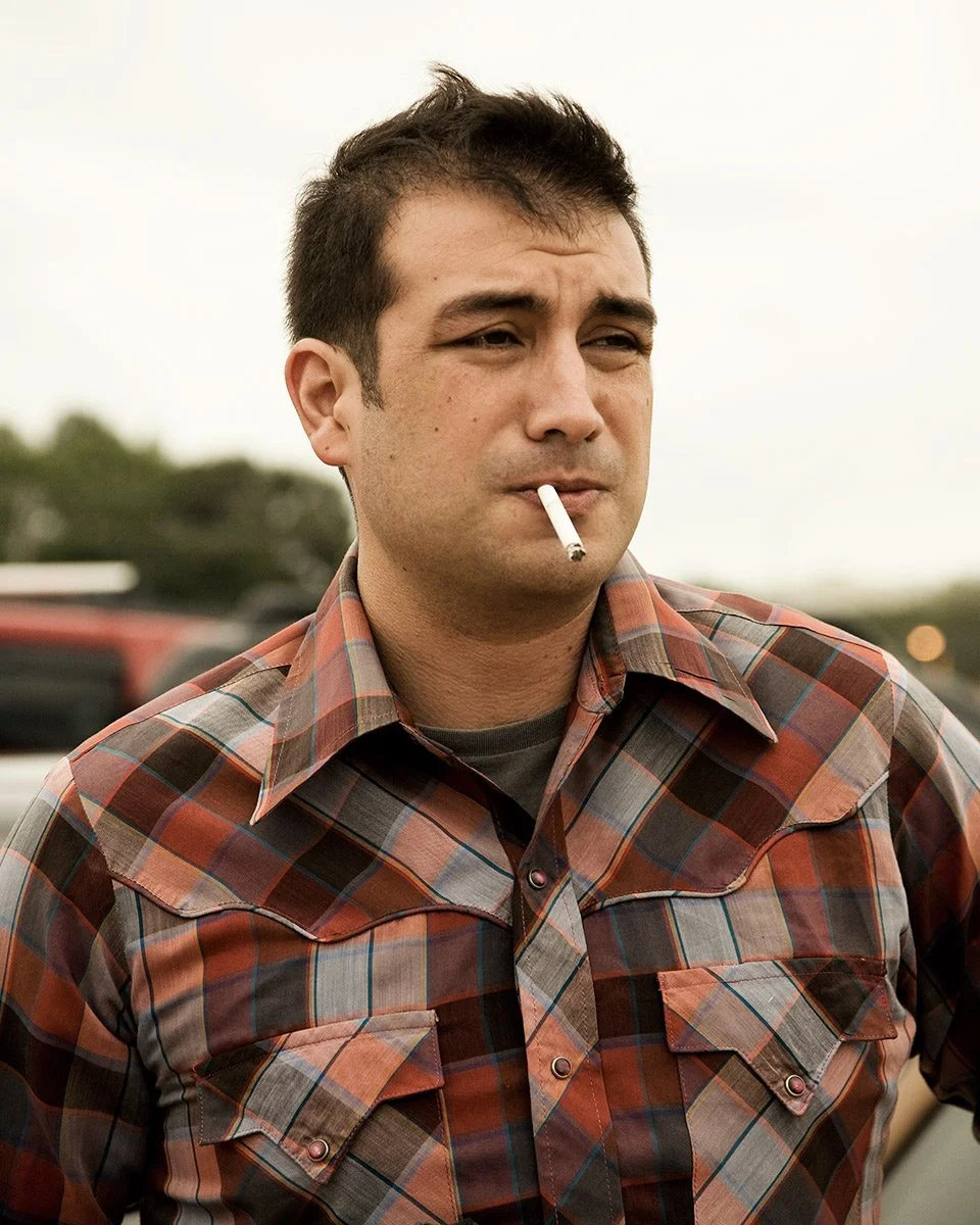 Editorial portrait of a man in a plaid shirt smoking a cigarette outdoors, photographed by Michael Rudin
