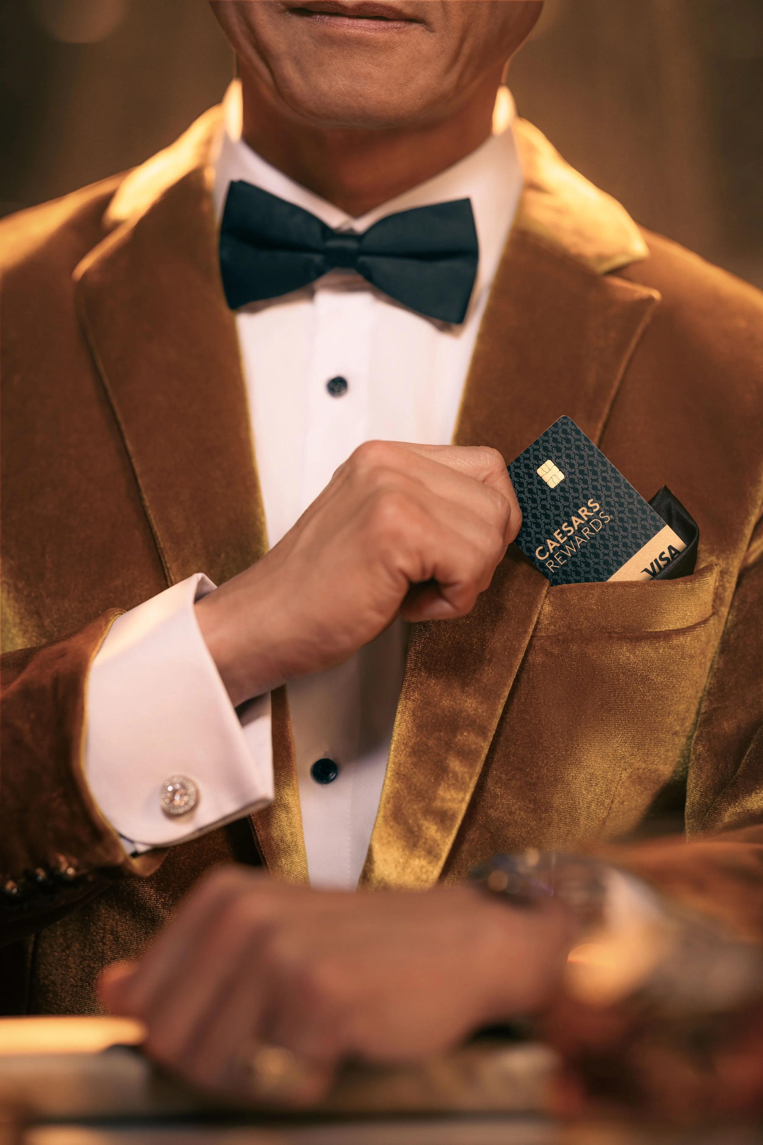 Man in gold tuxedo placing Caesars Rewards Visa card at blackjack table